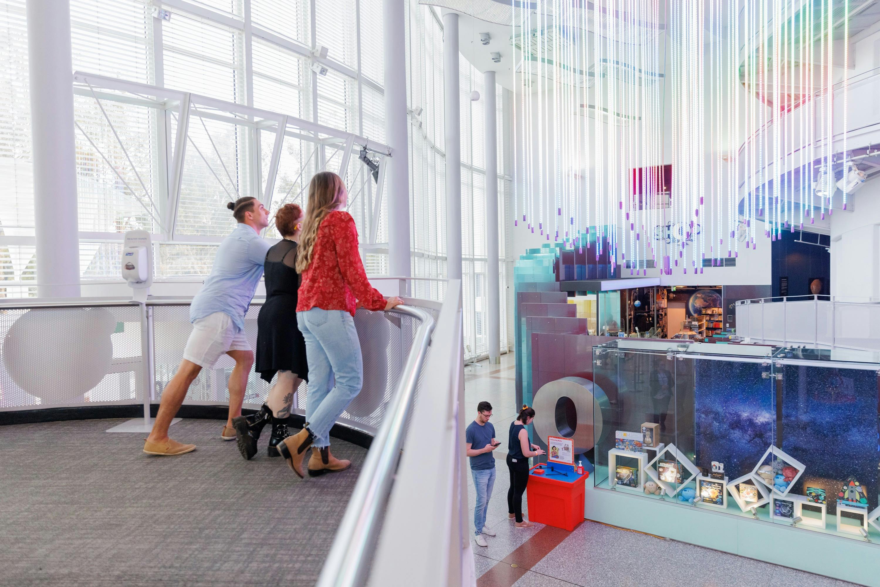 3 young people stand looking at a rainbow exhibit at Questacon