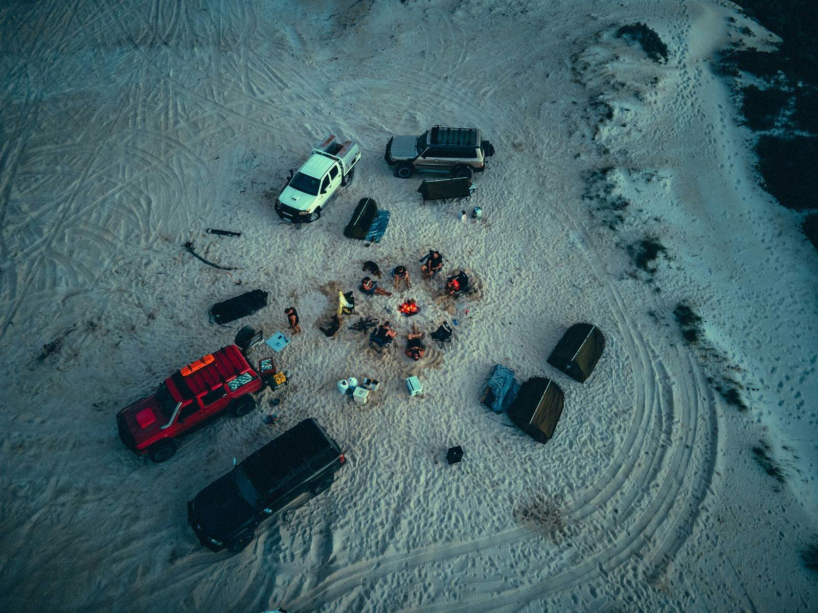 aerial view of people camped on the beach, sitting around a camp fire