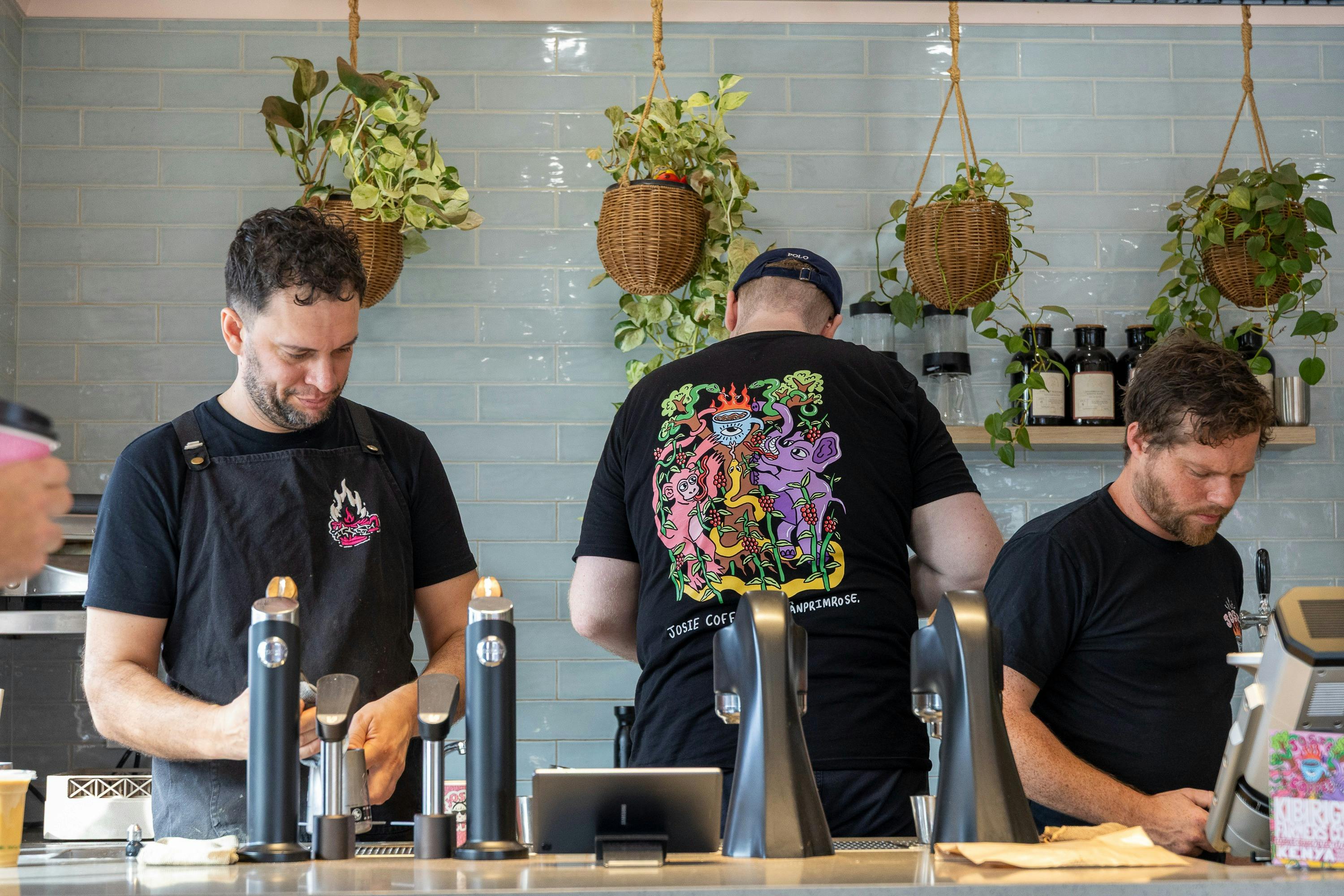 Three staff working behind a coffee machine. Their shirts show striking Josie branding.