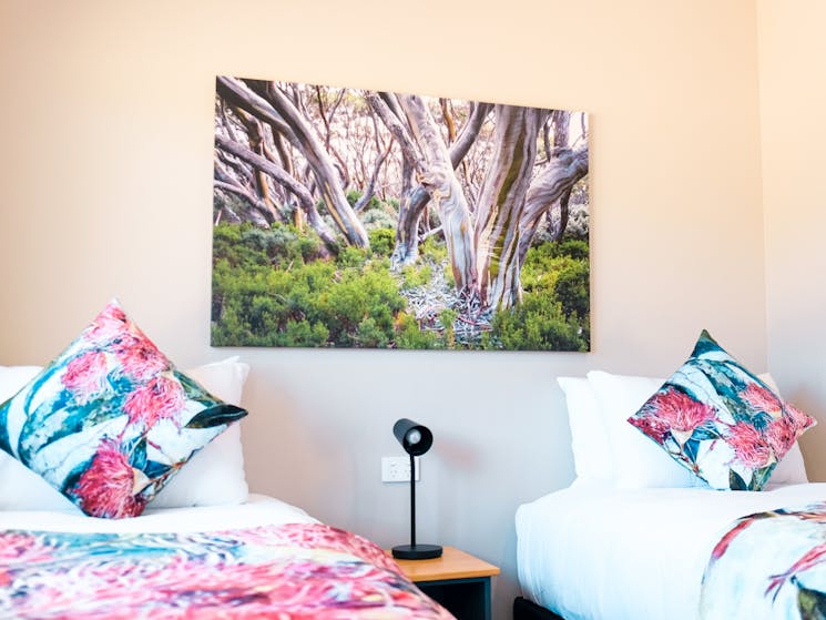Two single twin beds with a wooden side table between them. Nature print on the wall