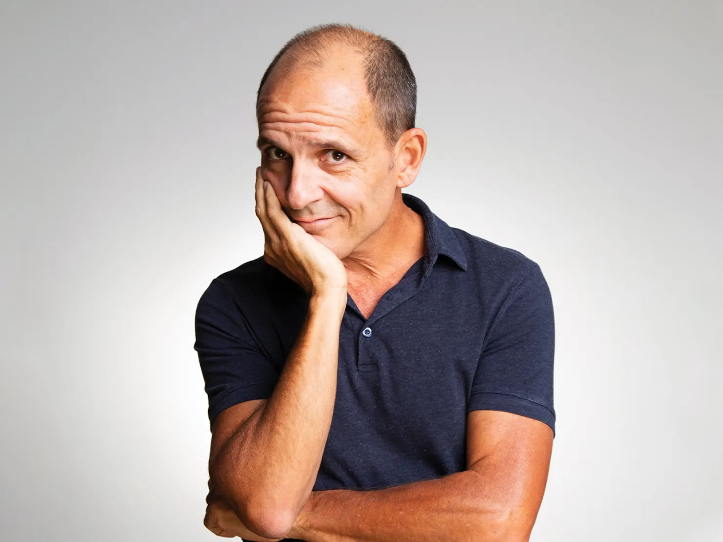 A bald middle aged man wearing navy blue short sleeve shirt.