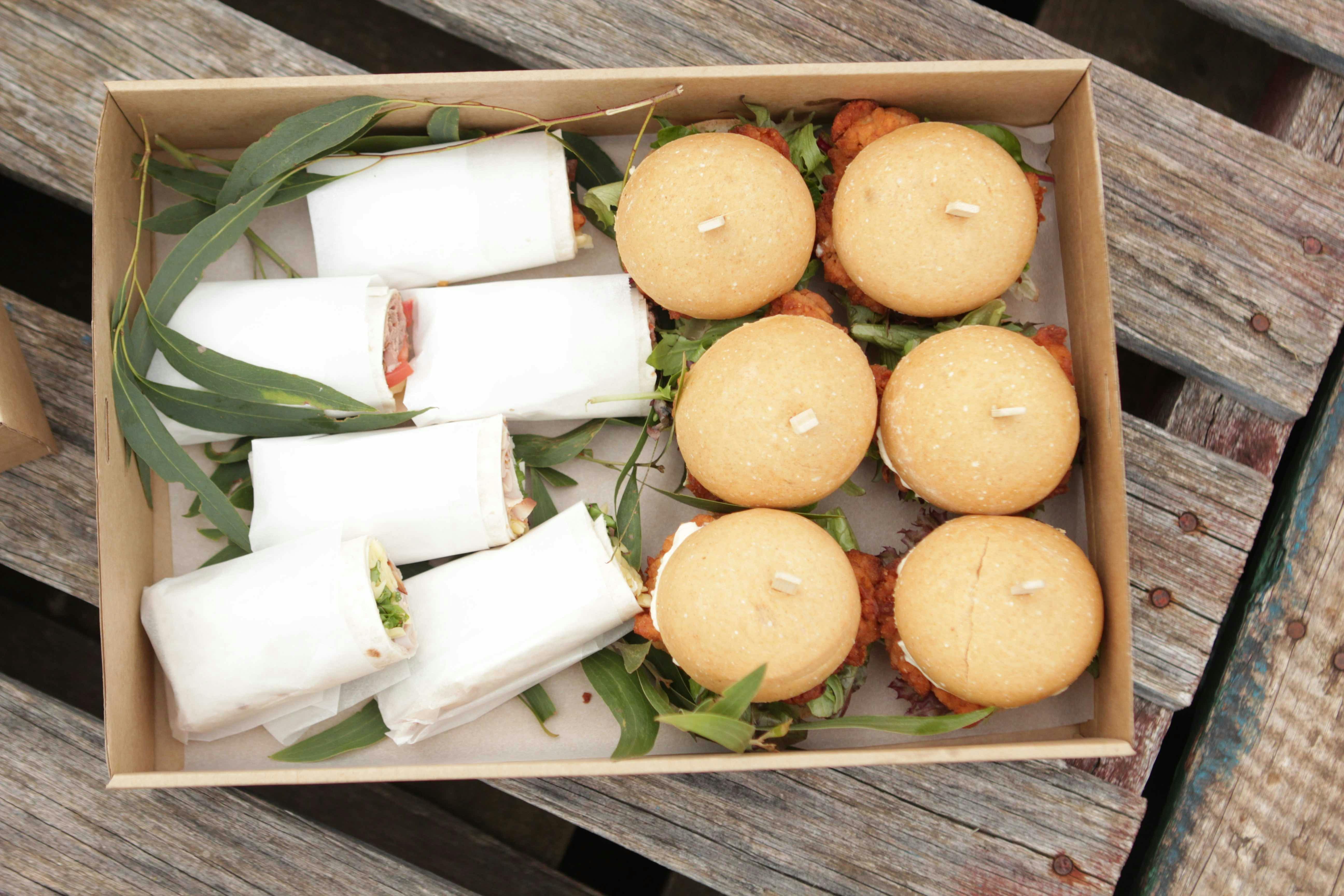 A platter box with sandwich wraps and burgers