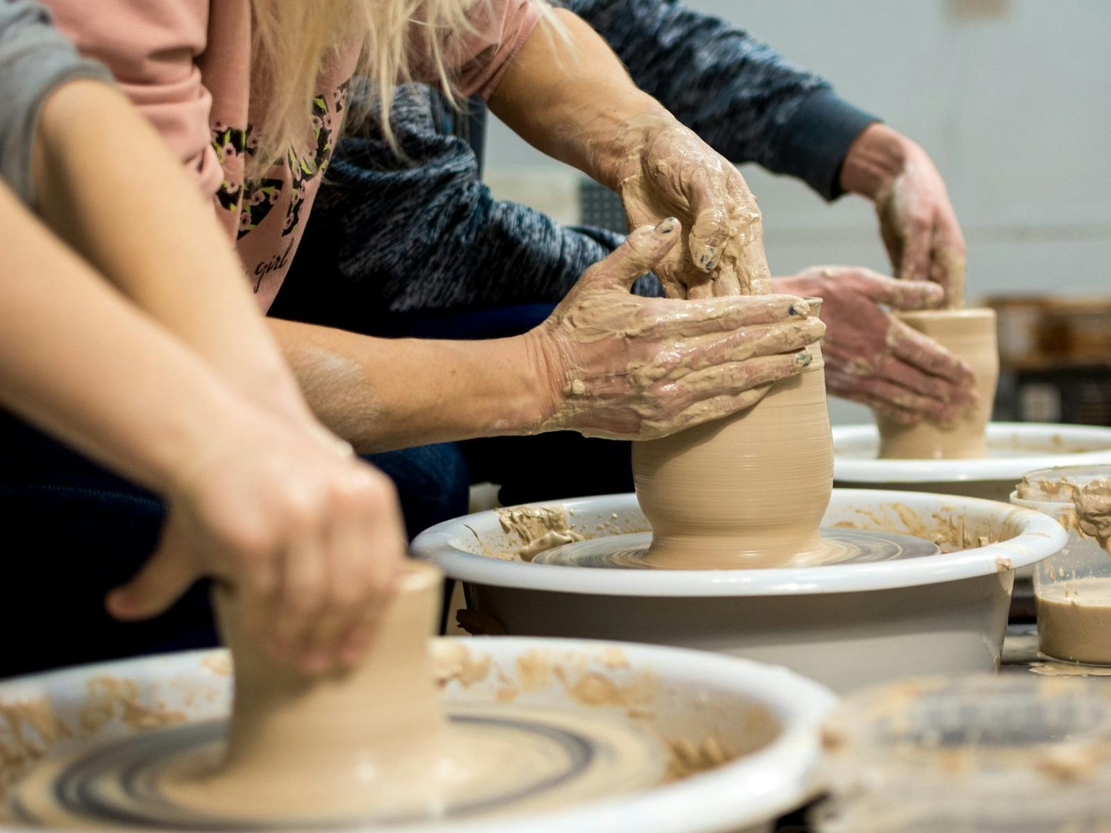 People leaning over and throwing clay bowls on a potter wheel