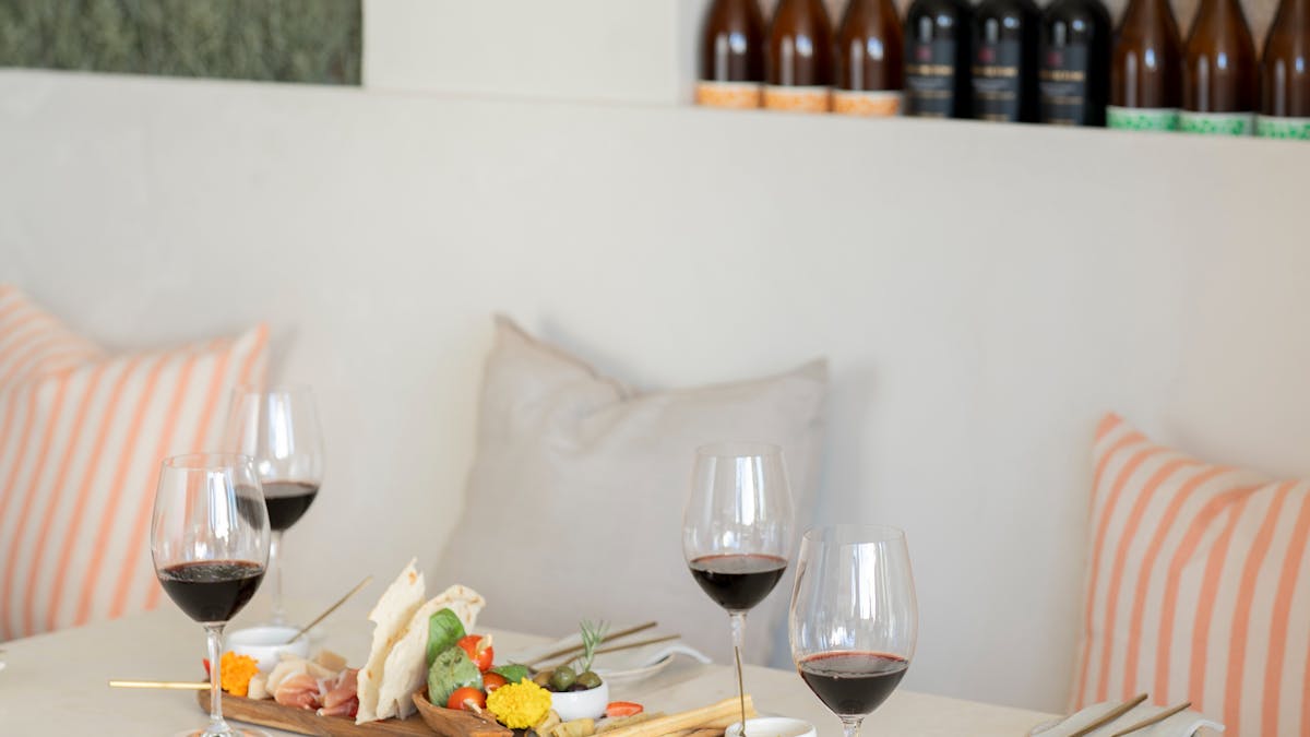 Charcuterie board with cured meats, cheeses, and accompaniments alongside four glasses of red wine o