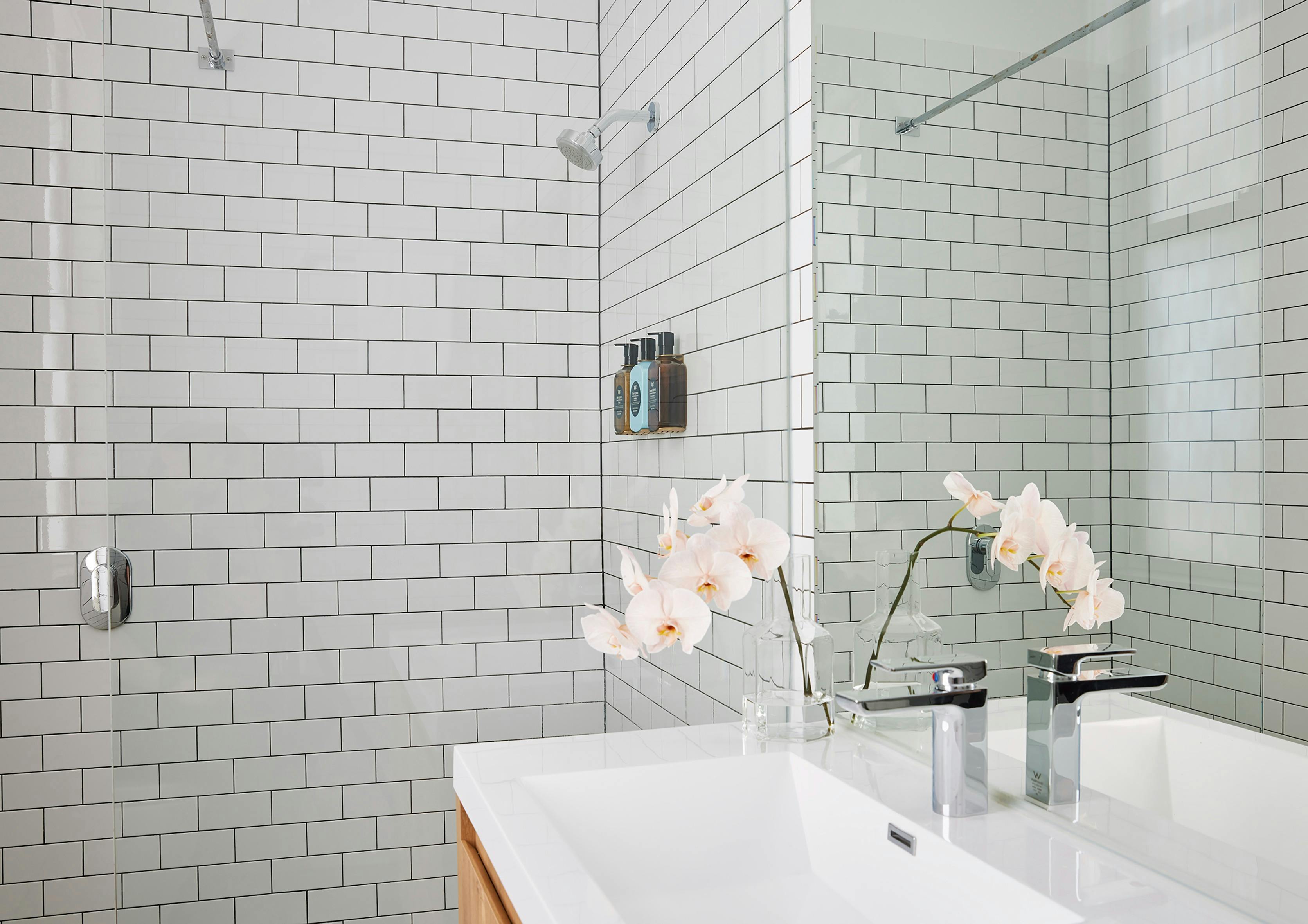 Bright bathroom with white subway tiles, glass shower, and modern vanity with orchid accents