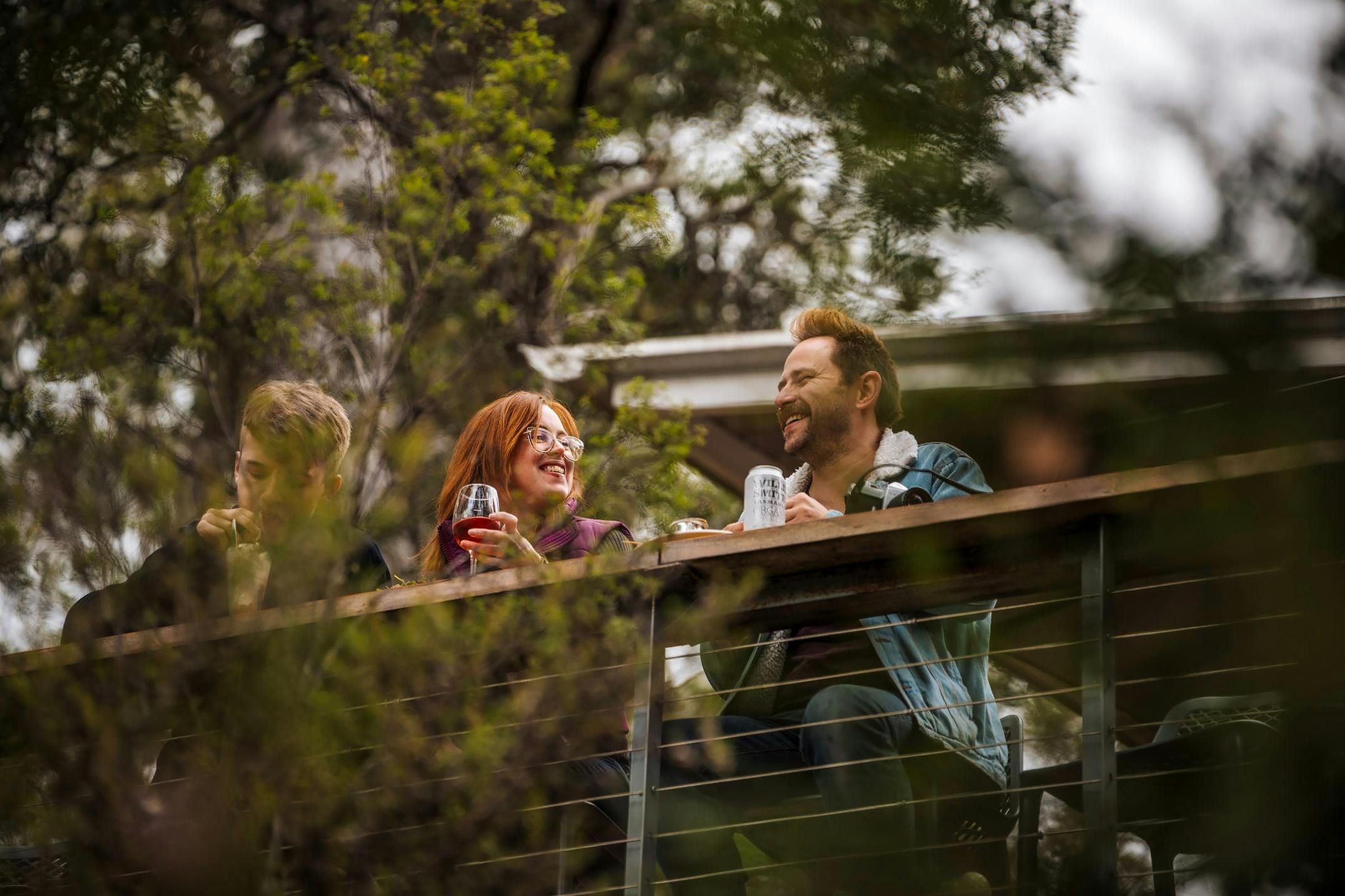 A couple sitting on a deck overlooking the river and forest, smiling and enjoying a meal