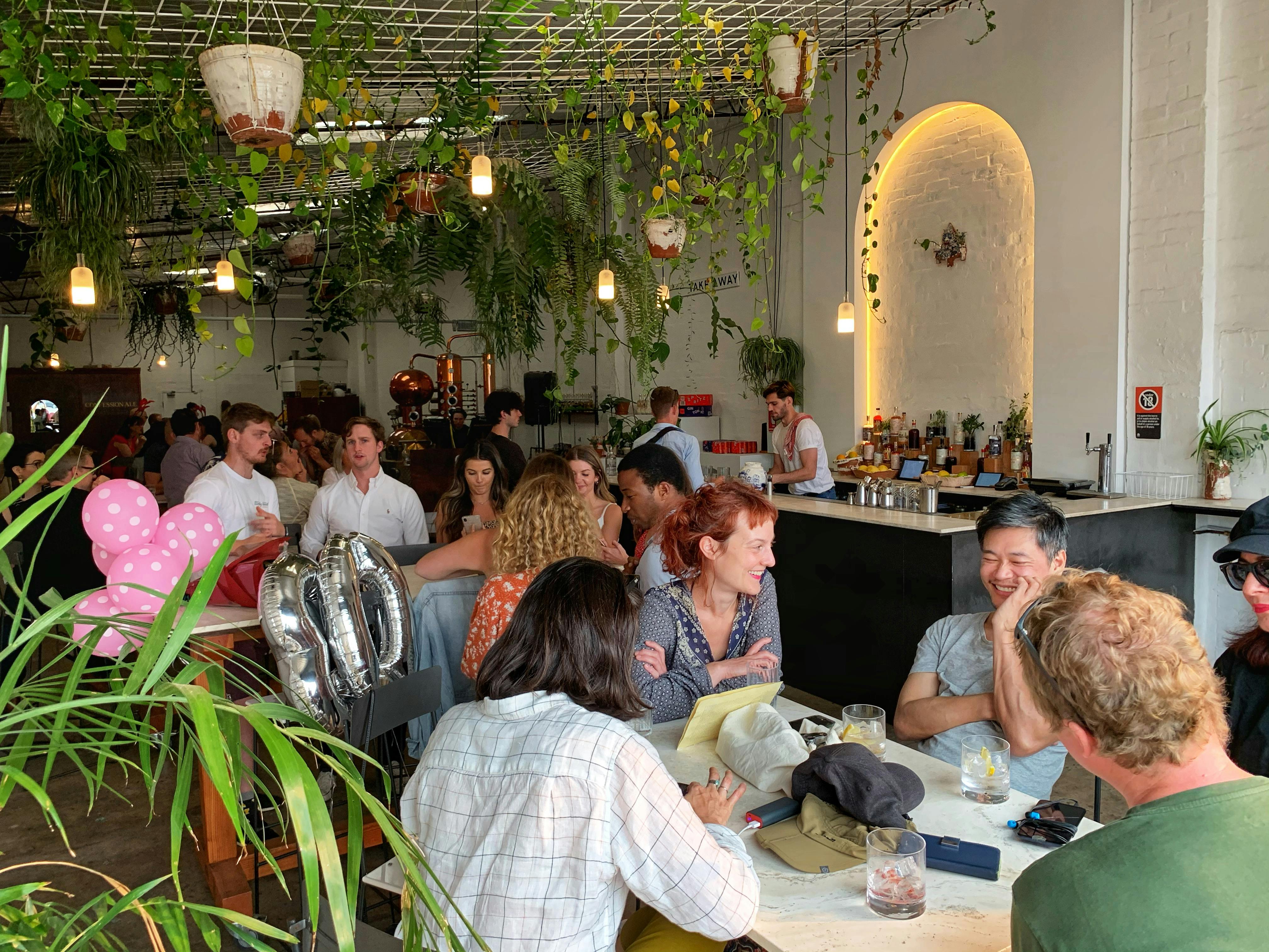 ID Lots of people looking happy and chatting at tables inside the Gin Distillery