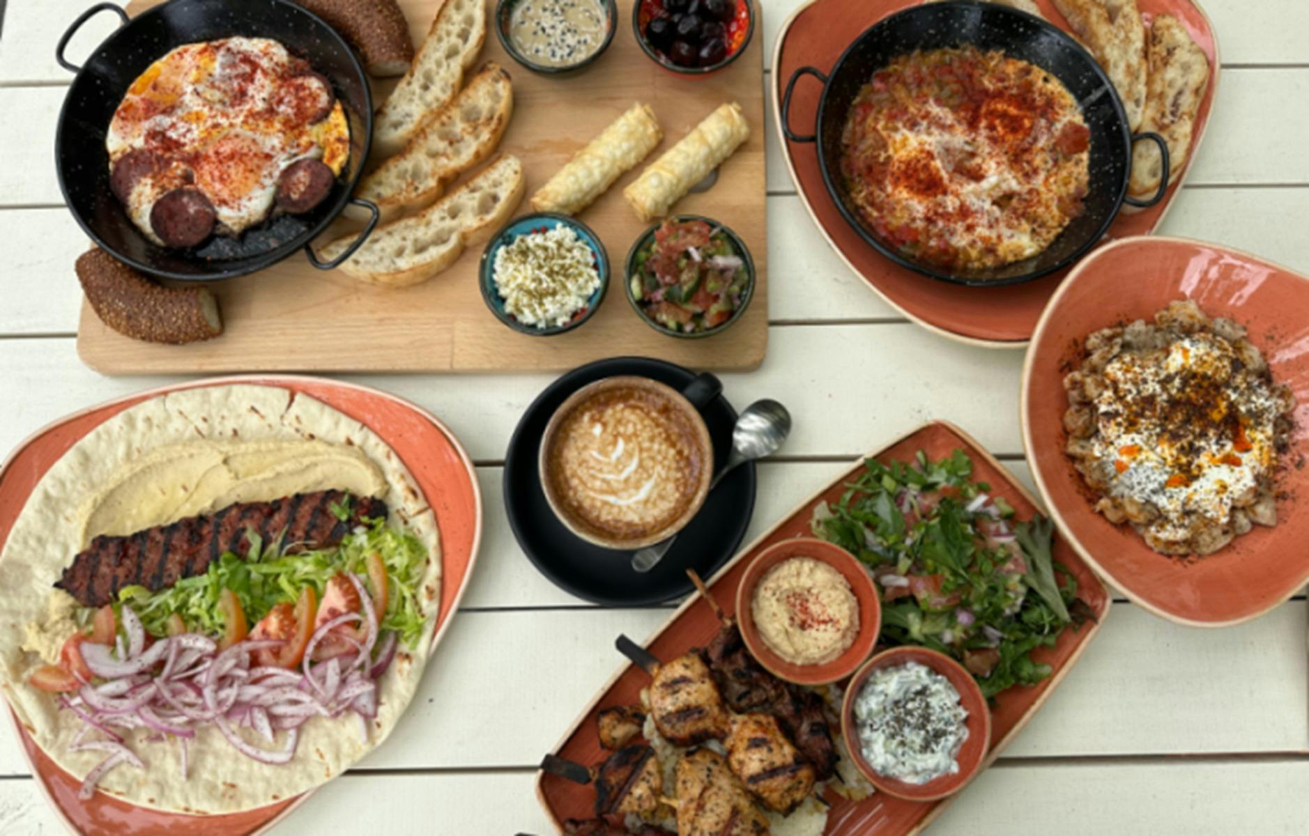 Array of Cafe Cultura offerings, including salad wraps and coffee, on white wooden table.