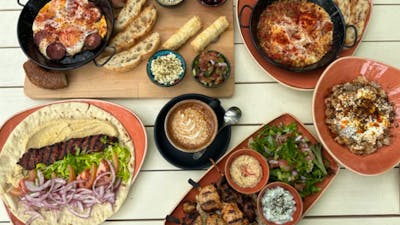 Array of Cafe Cultura offerings, including salad wraps and coffee, on white wooden table.