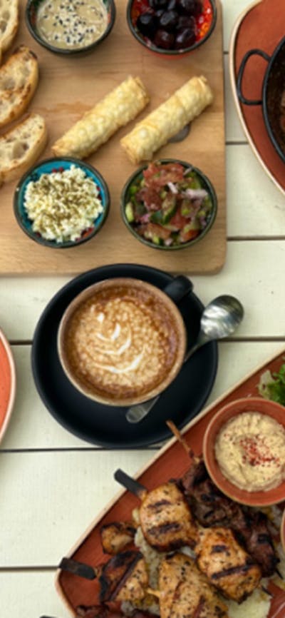 Array of Cafe Cultura offerings, including salad wraps and coffee, on white wooden table.