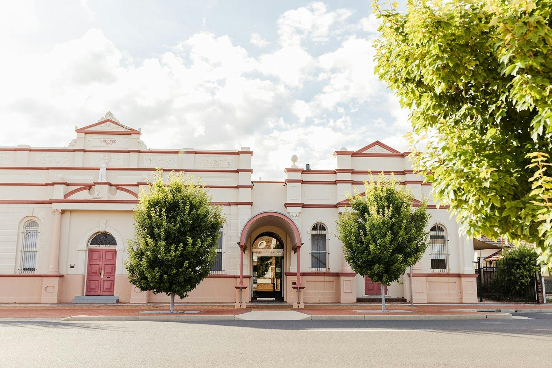 Front of Art Gallery with entrance in the middle and a tree on either side of the entrance awning