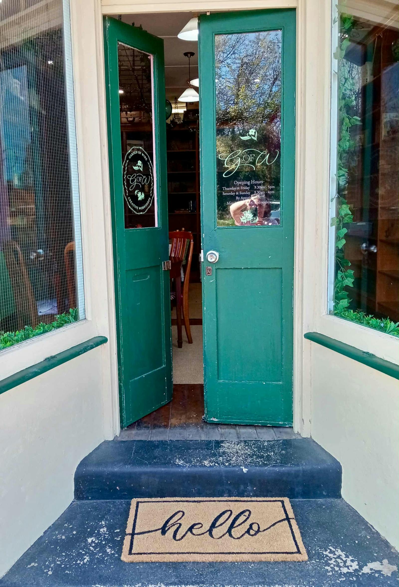Pair of green doors with one open. Two low steps with a hello door mat.