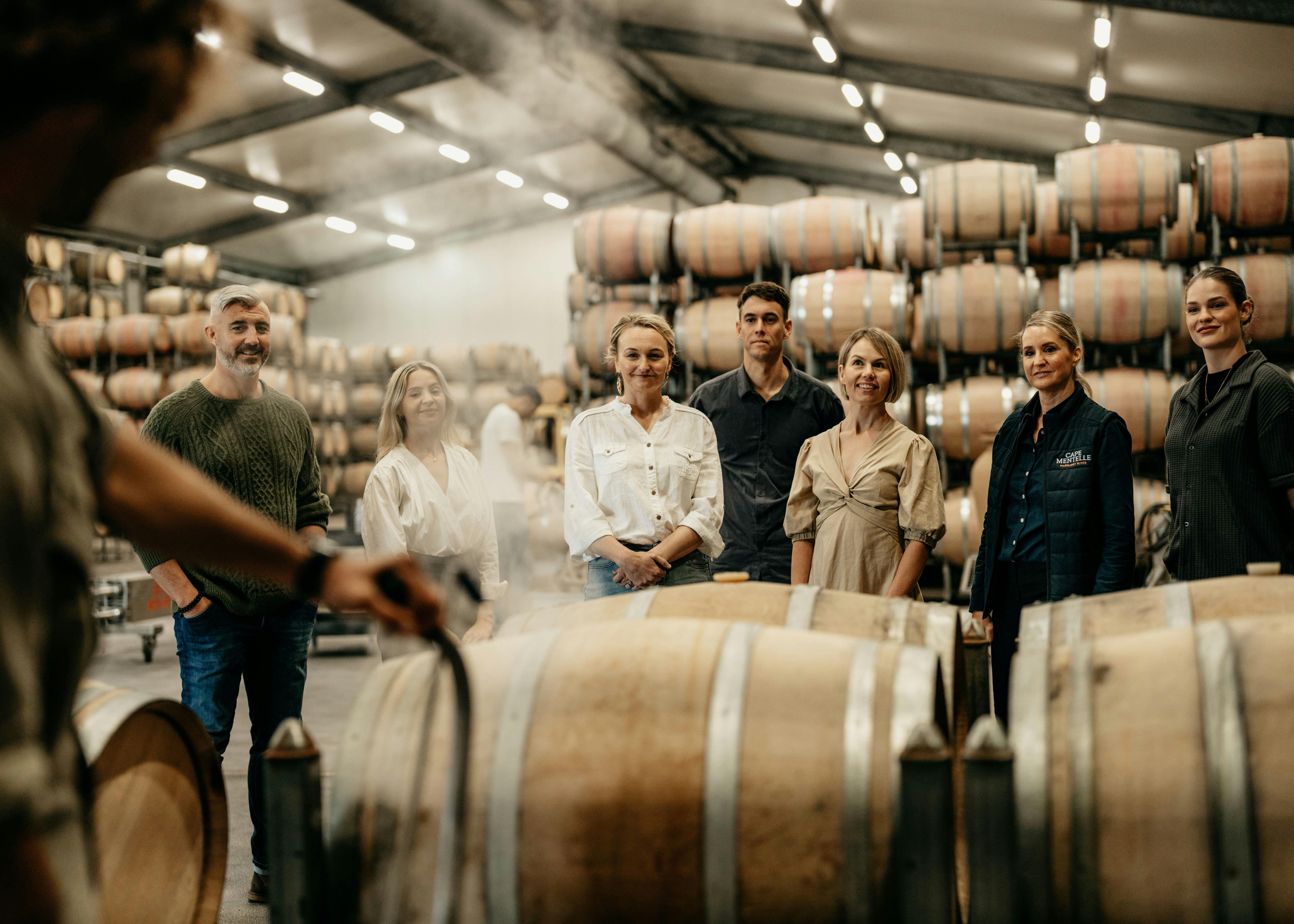 7 guests and a host stand behind barrels as a staff member demonstrates the steaming process