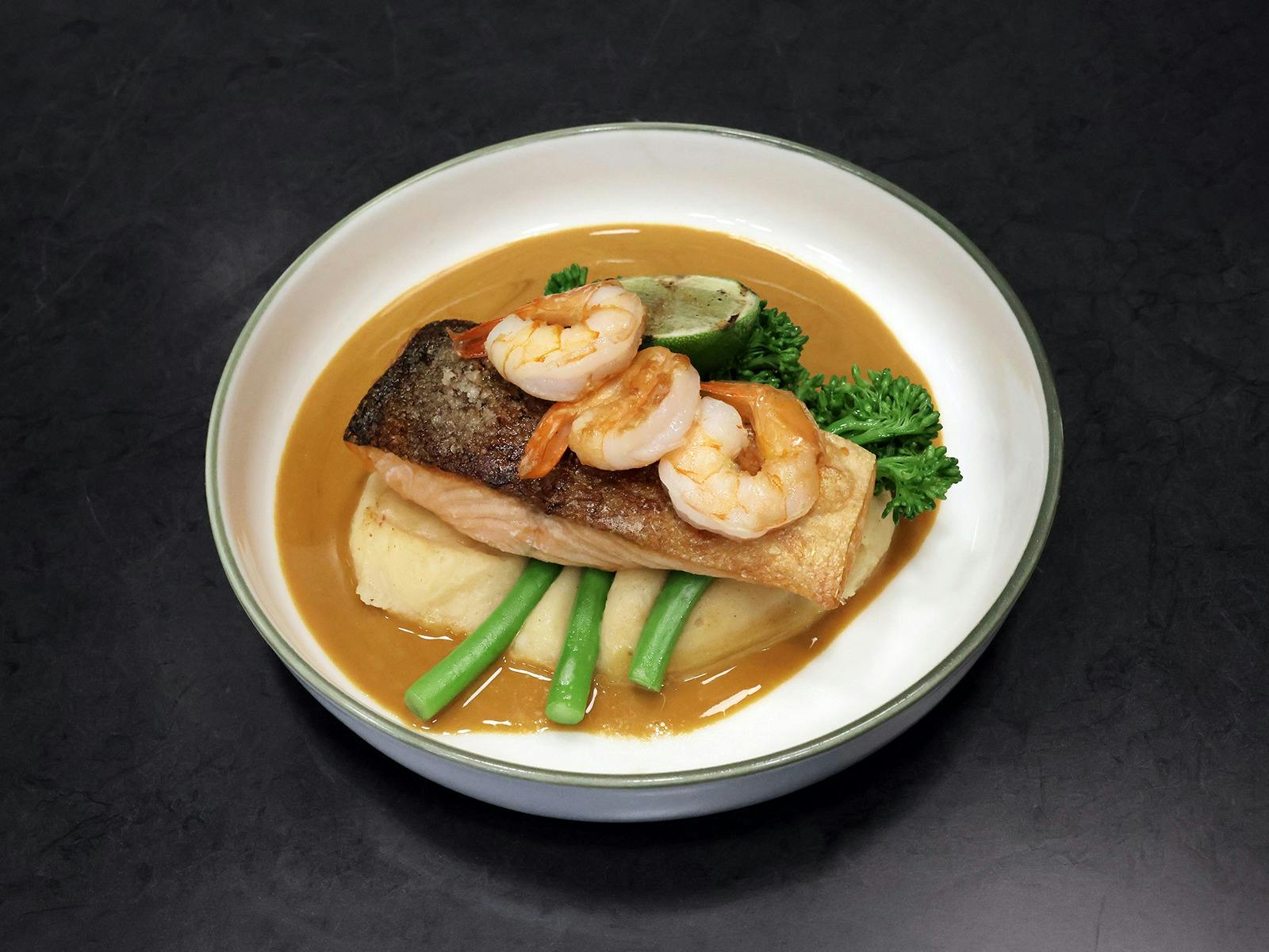 Baked Atlantic salmon with sweet potato mash, broccolini, garlic prawns and sauce in a white bowl.