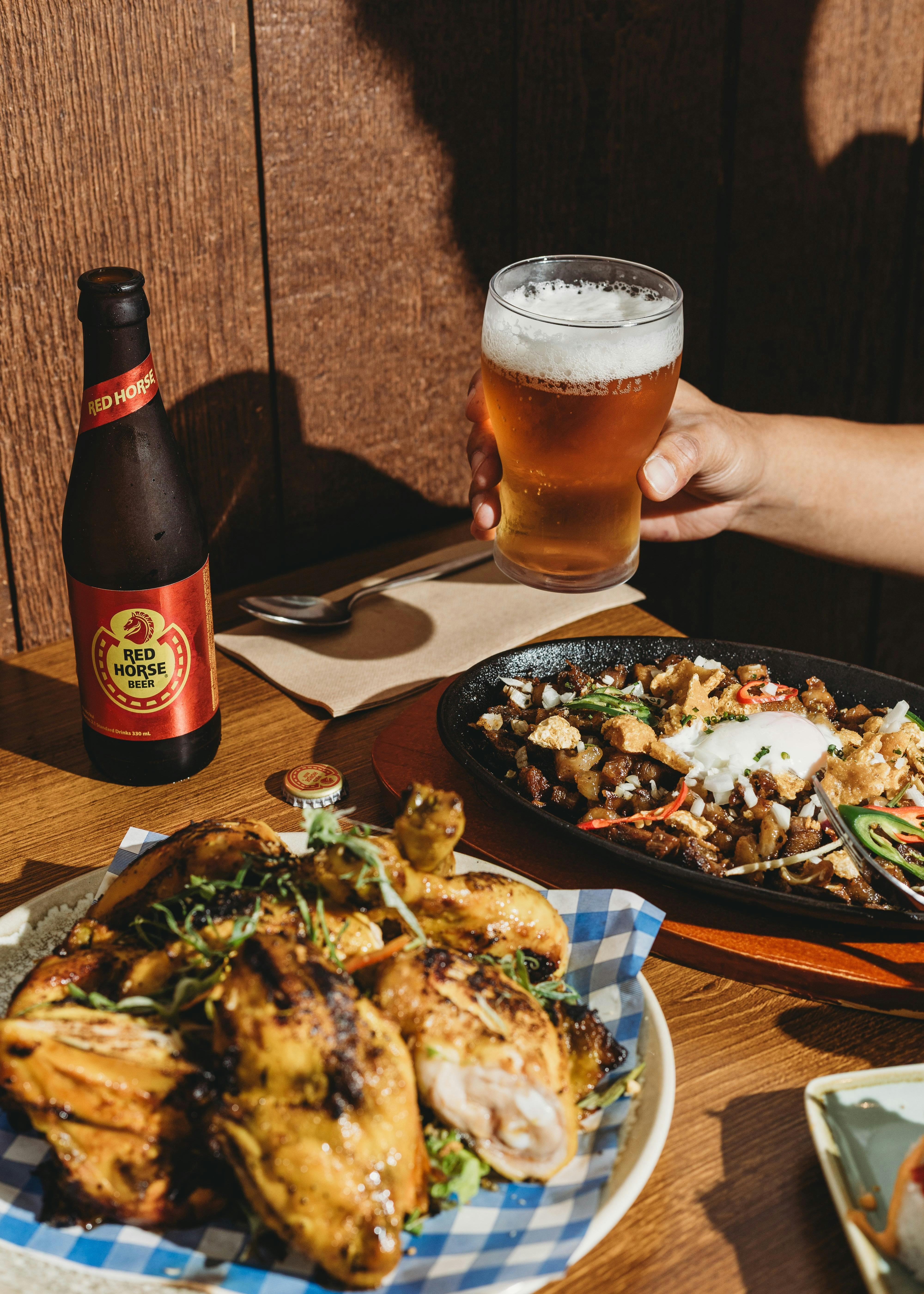 A table with Filipino dishes including grilled pork, sizzling sisig topped with an egg and chili, a