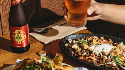 A table with Filipino dishes including grilled pork, sizzling sisig topped with an egg and chili, a