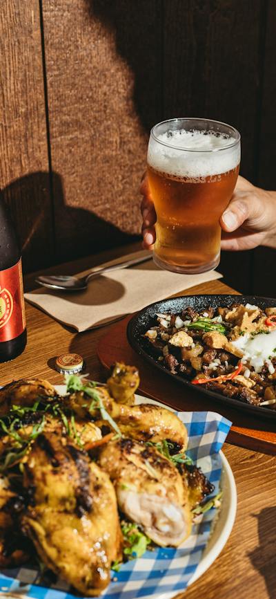 A table with Filipino dishes including grilled pork, sizzling sisig topped with an egg and chili, a