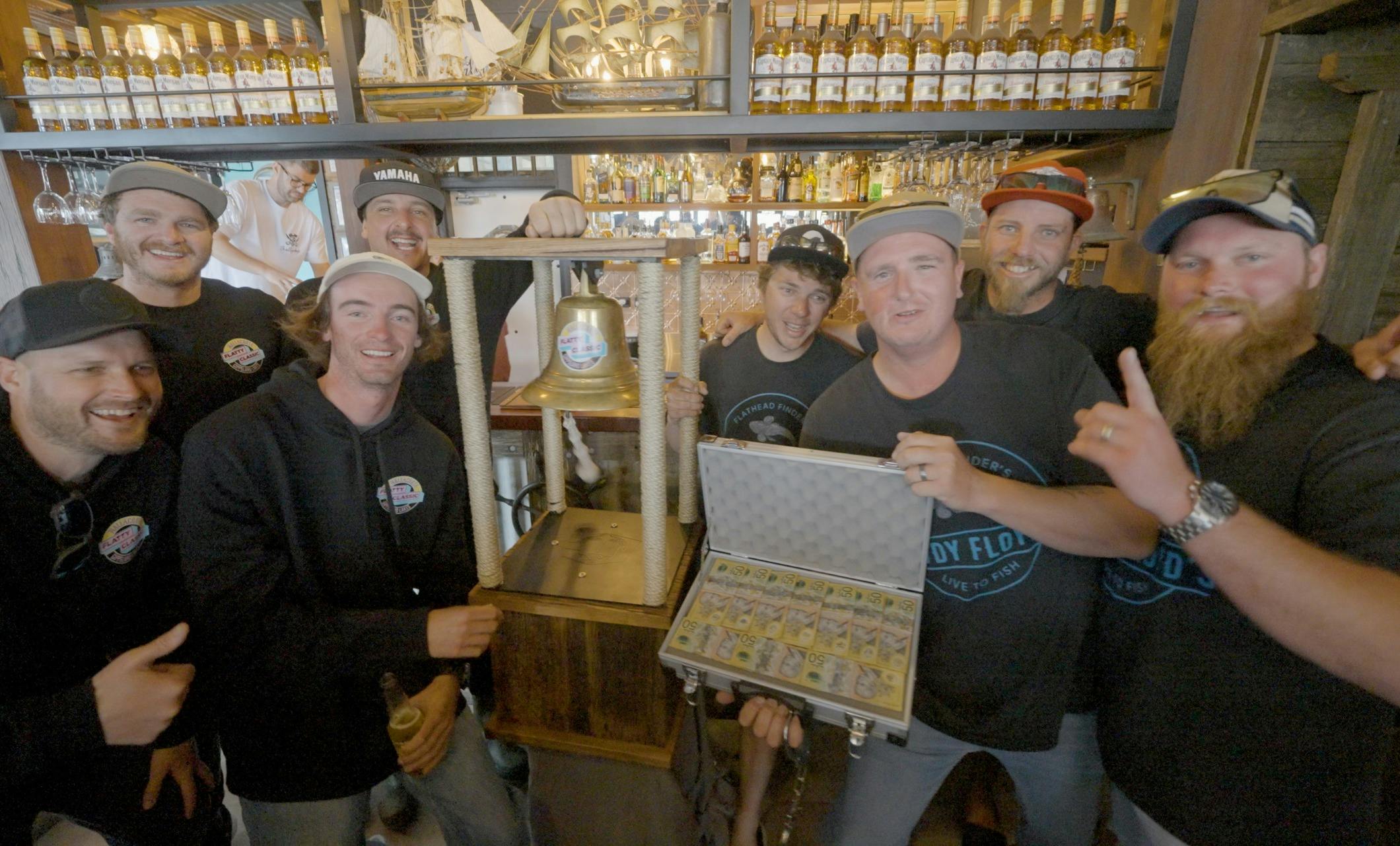 Winning team celebrating at the bar with the Flatty Classic trophy bell and prize case