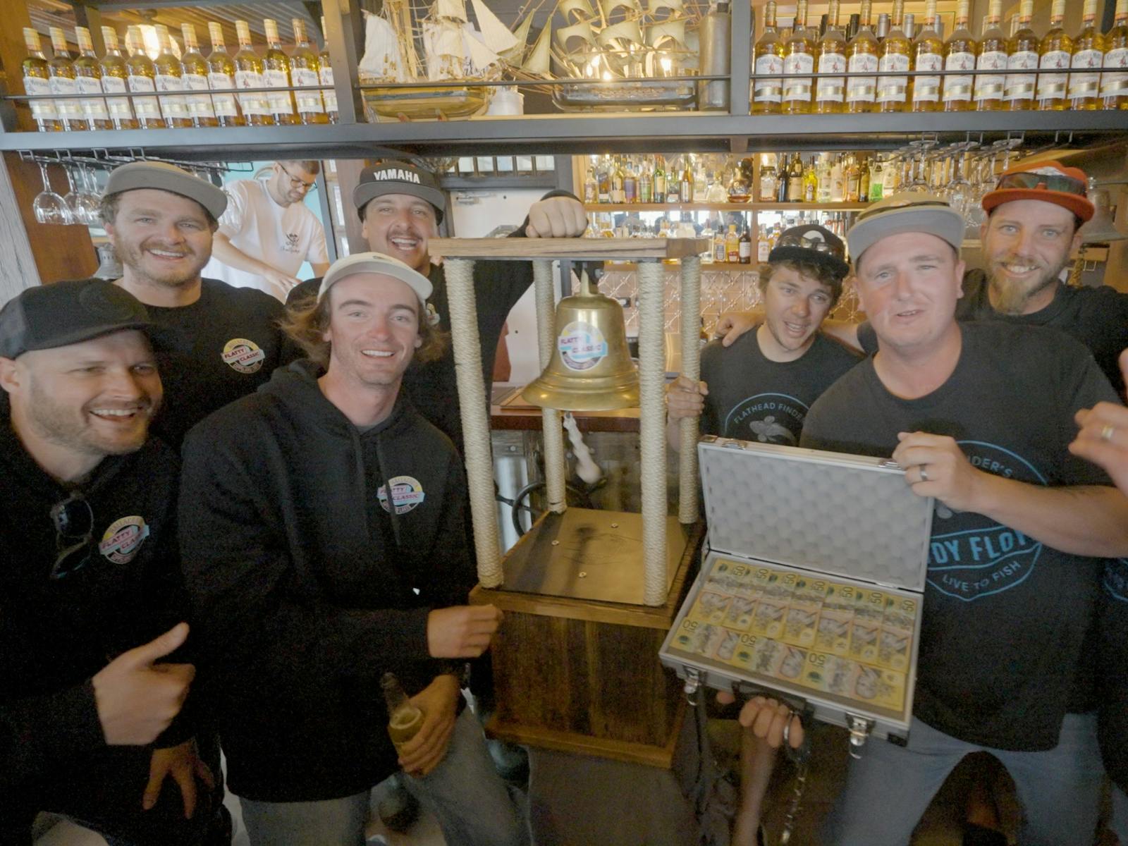 Winning team celebrating at the bar with the Flatty Classic trophy bell and prize case