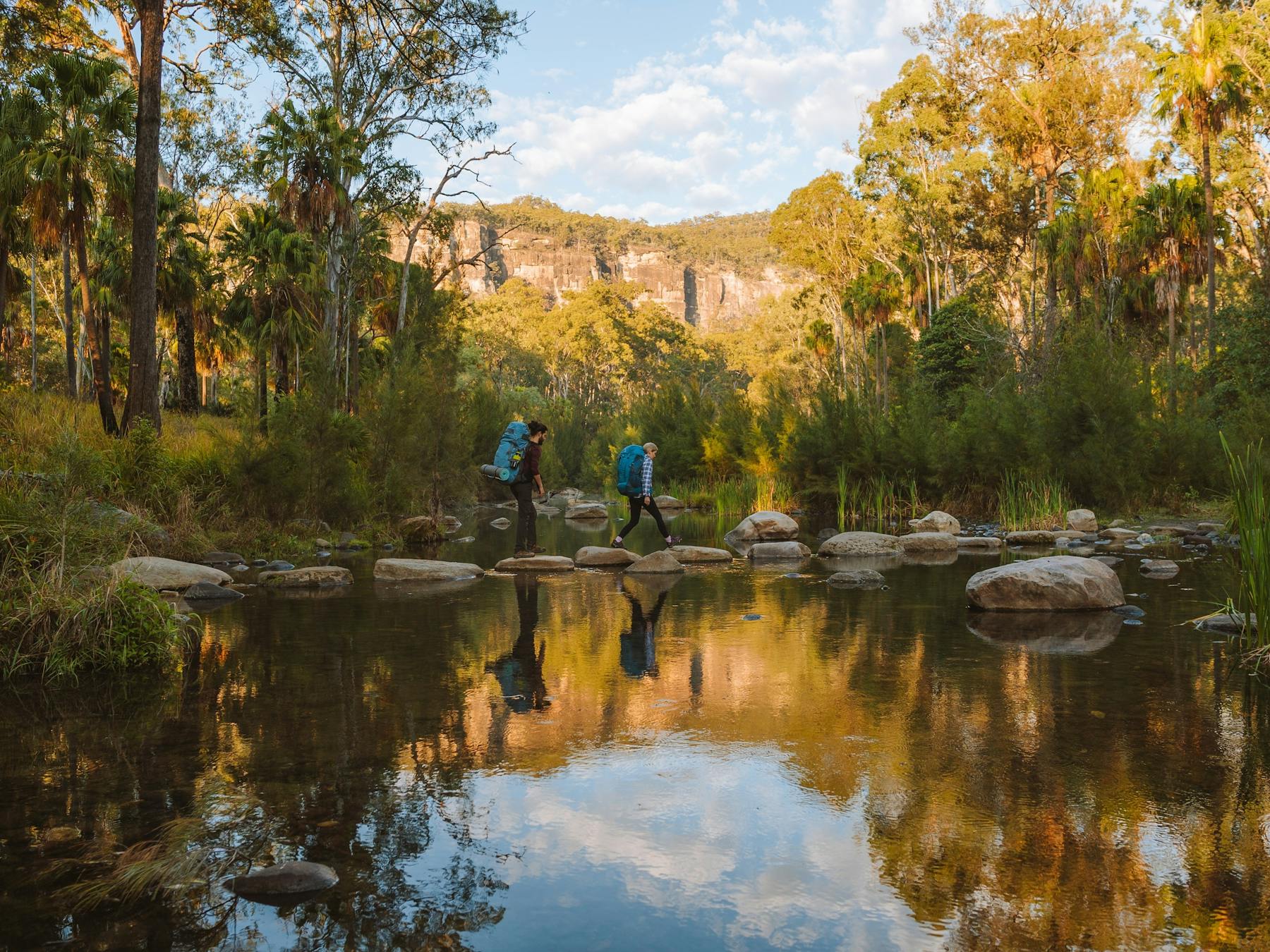 Two hikers walking over rock path placed in water.