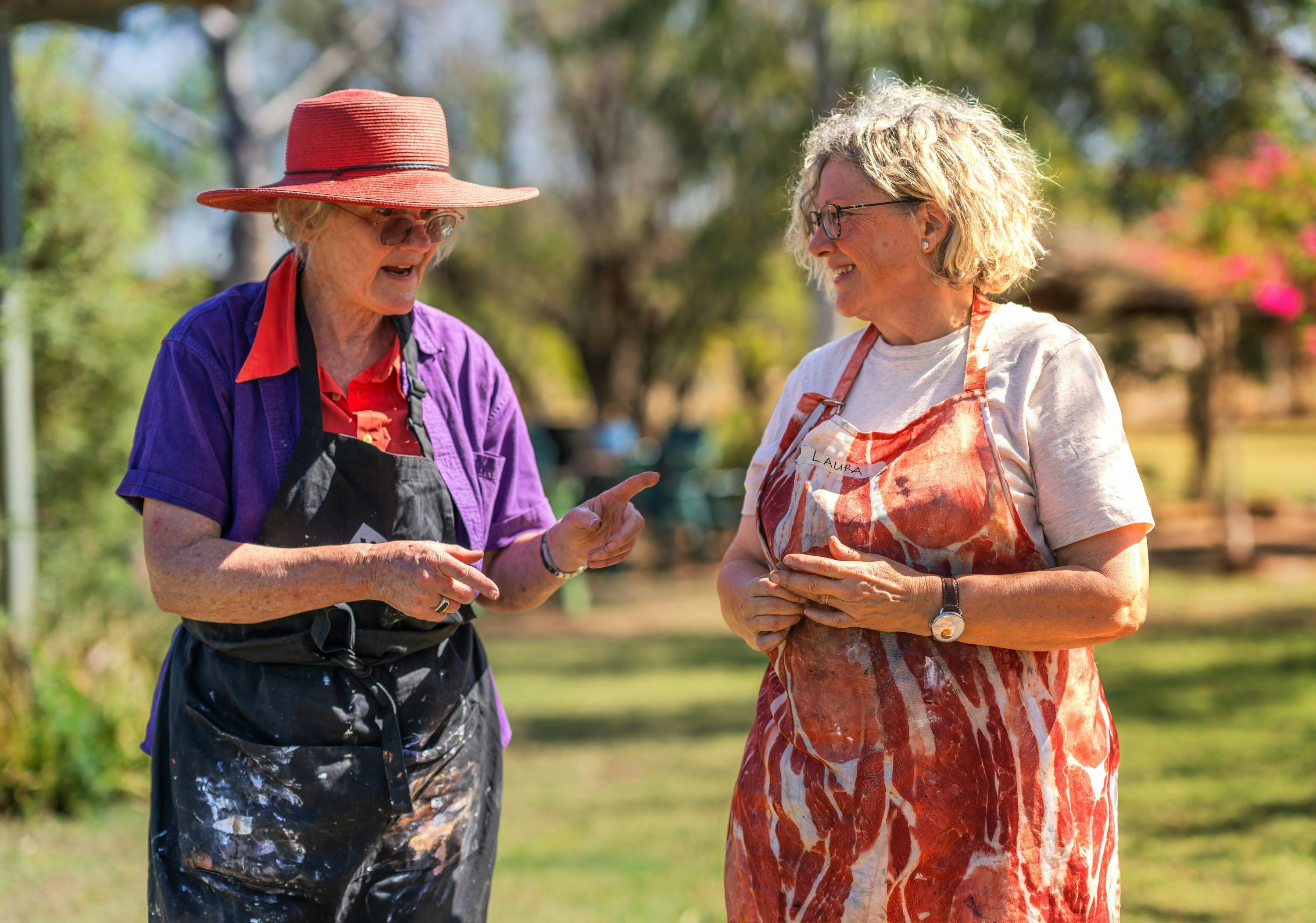 Woman in red hat walking and talking to another woman in an apron