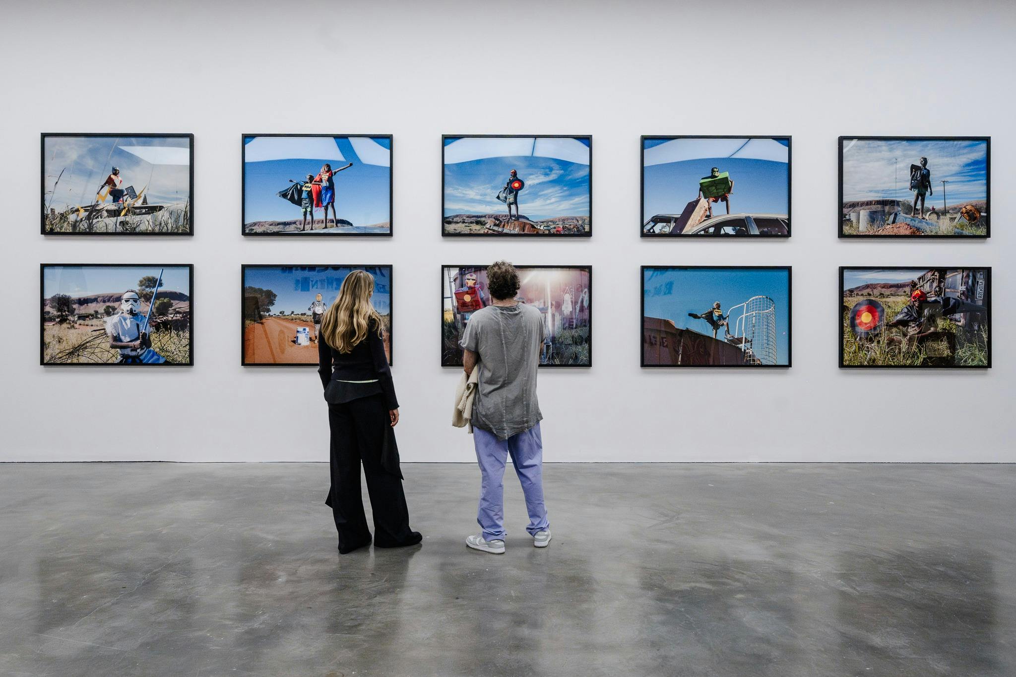 Two people observe ten photographs of children assuming superhero poses