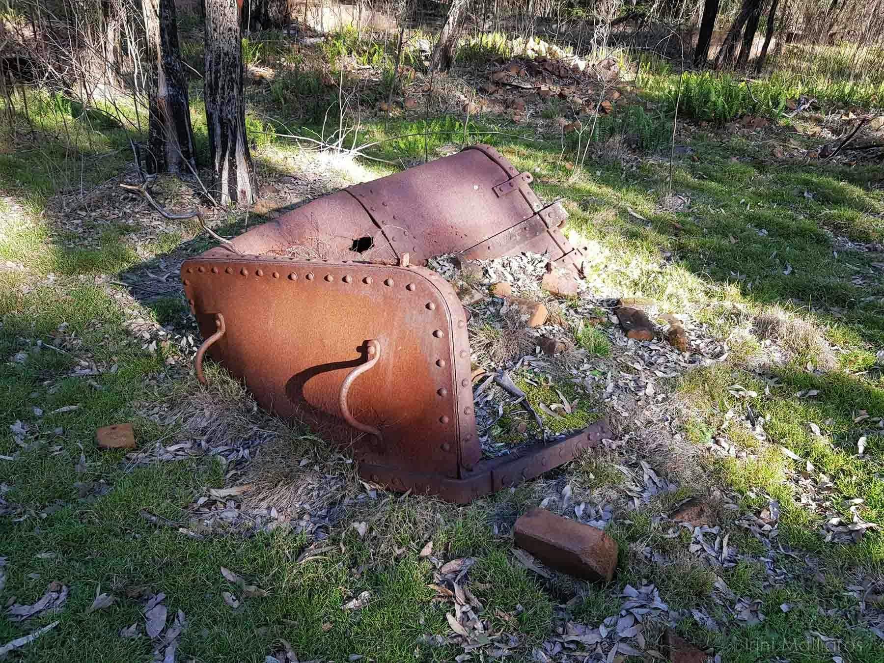 Squashed rusting container covered in some rubble in the bush illumimated by filtered sunlight