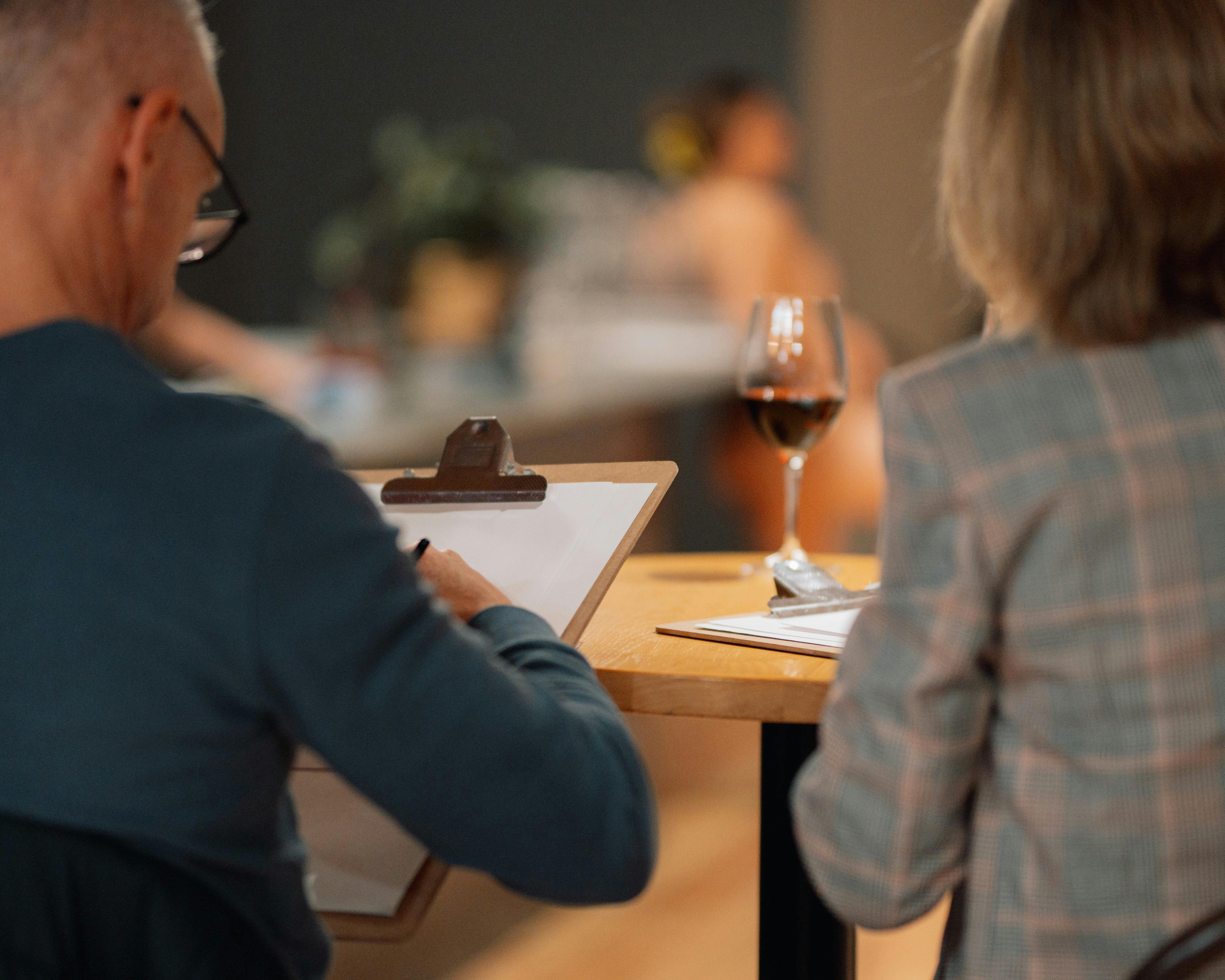 Two people drawing, with a glass of red wine on the table
