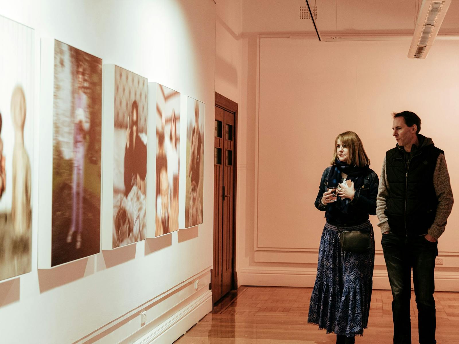 Two people, standing in Gallery One, viewing photographic works by Lauren Dunn.