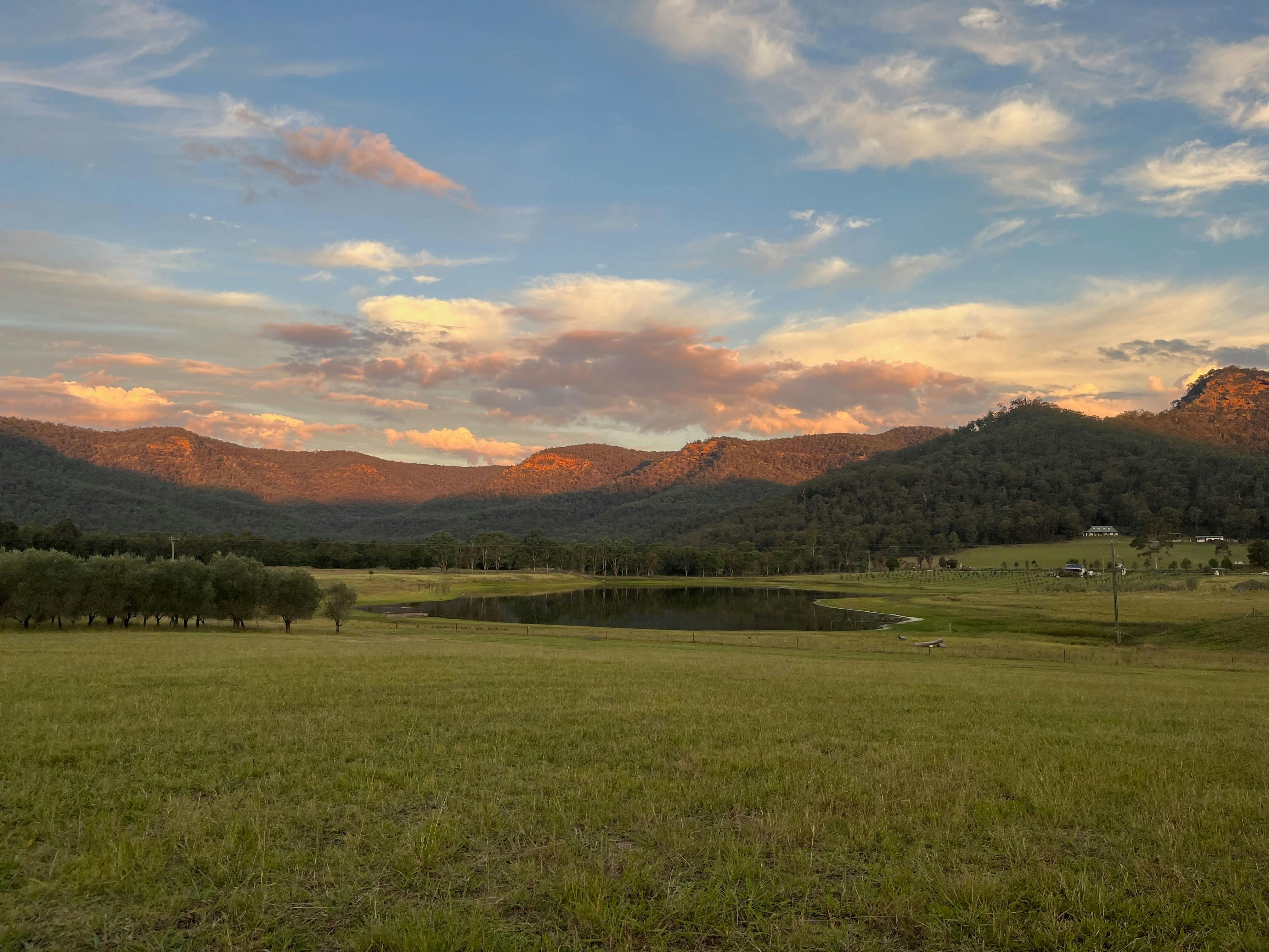 landscape featuring farm, billabong and mountains in setting sunlight