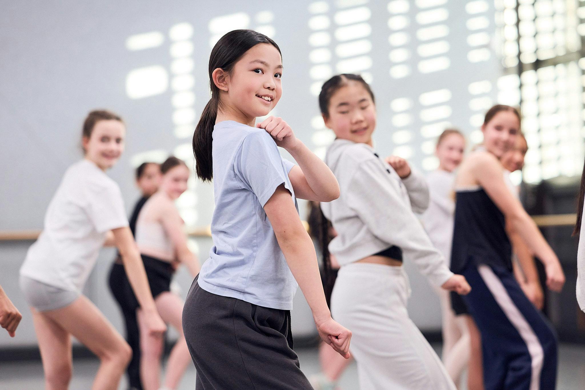 Young female is dancing in a class. There are other dancers around her.