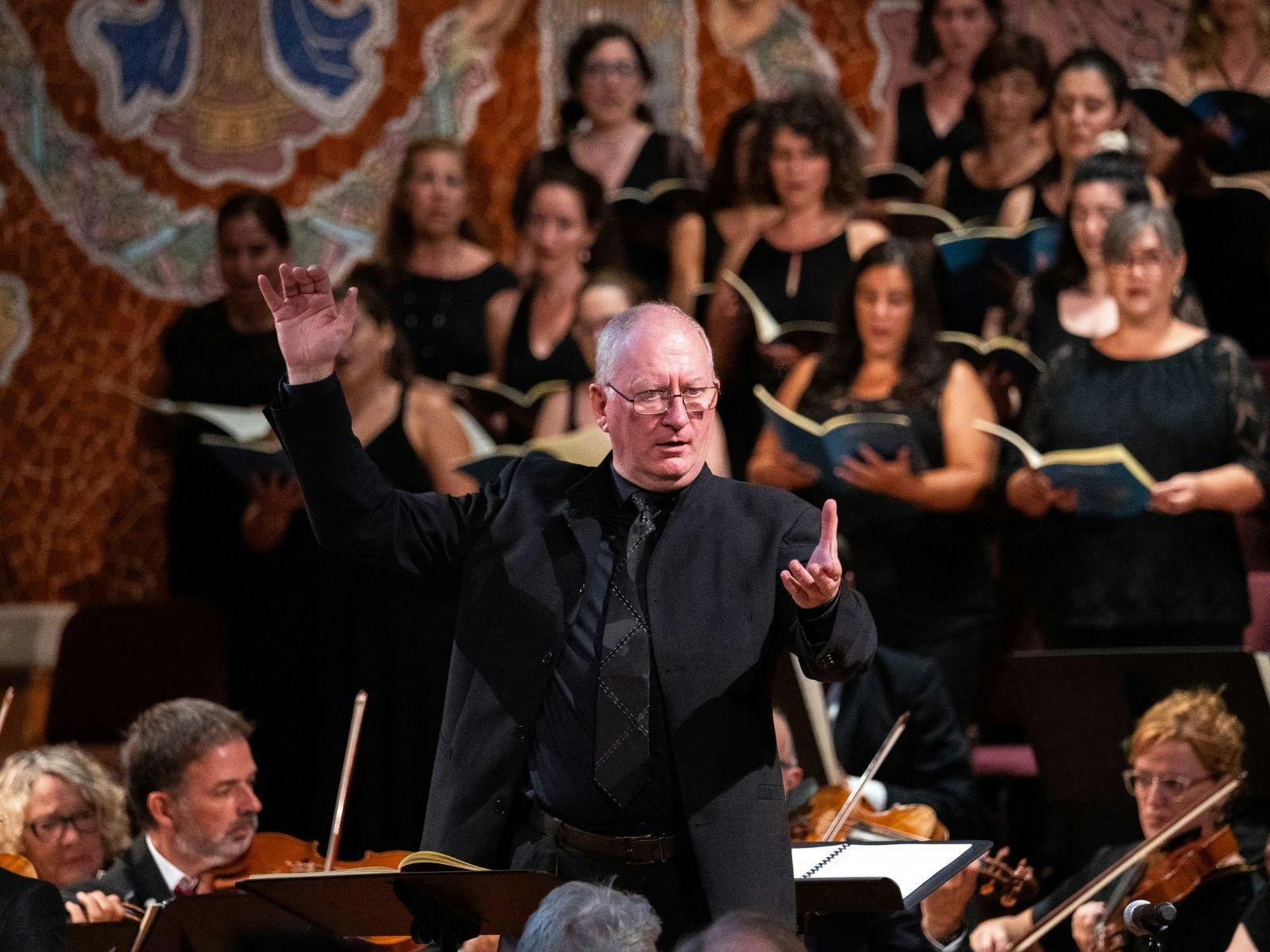 Conductor leading a choir and orchestra in an ornate concert hall with mosaic walls