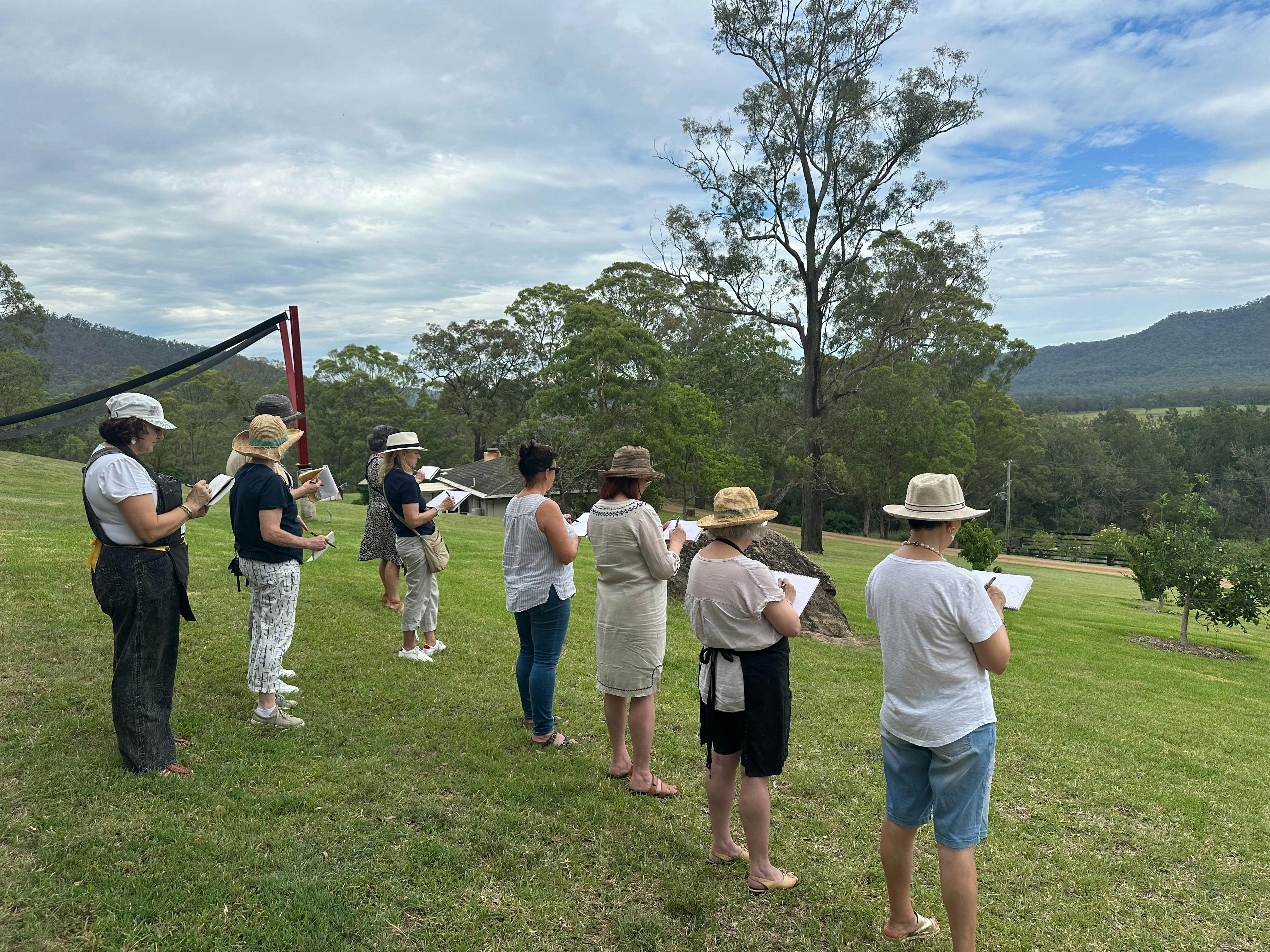 a group of artists stand lined up on a hill sketching the view