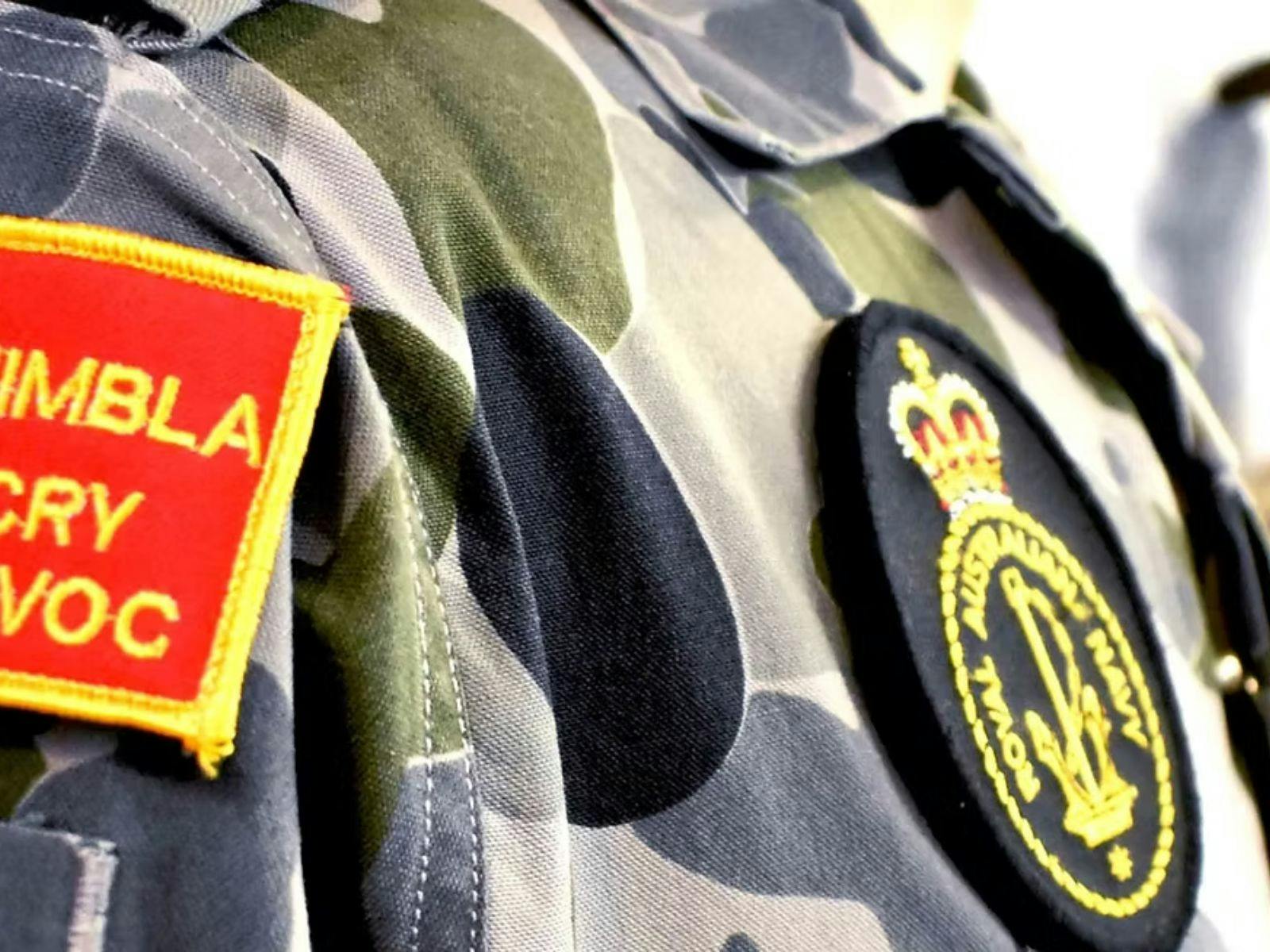 Close-up of a camouflage naval uniform featuring embroidered naval badges and patches.