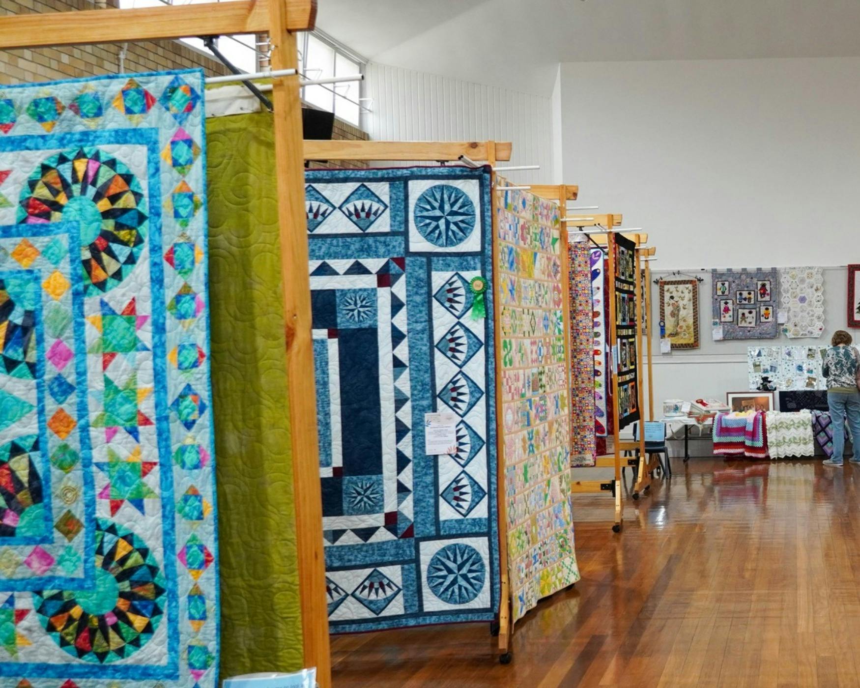 Main Display of Qilts and raft in Hall. Quits are hanging from frames and craft is on the back table