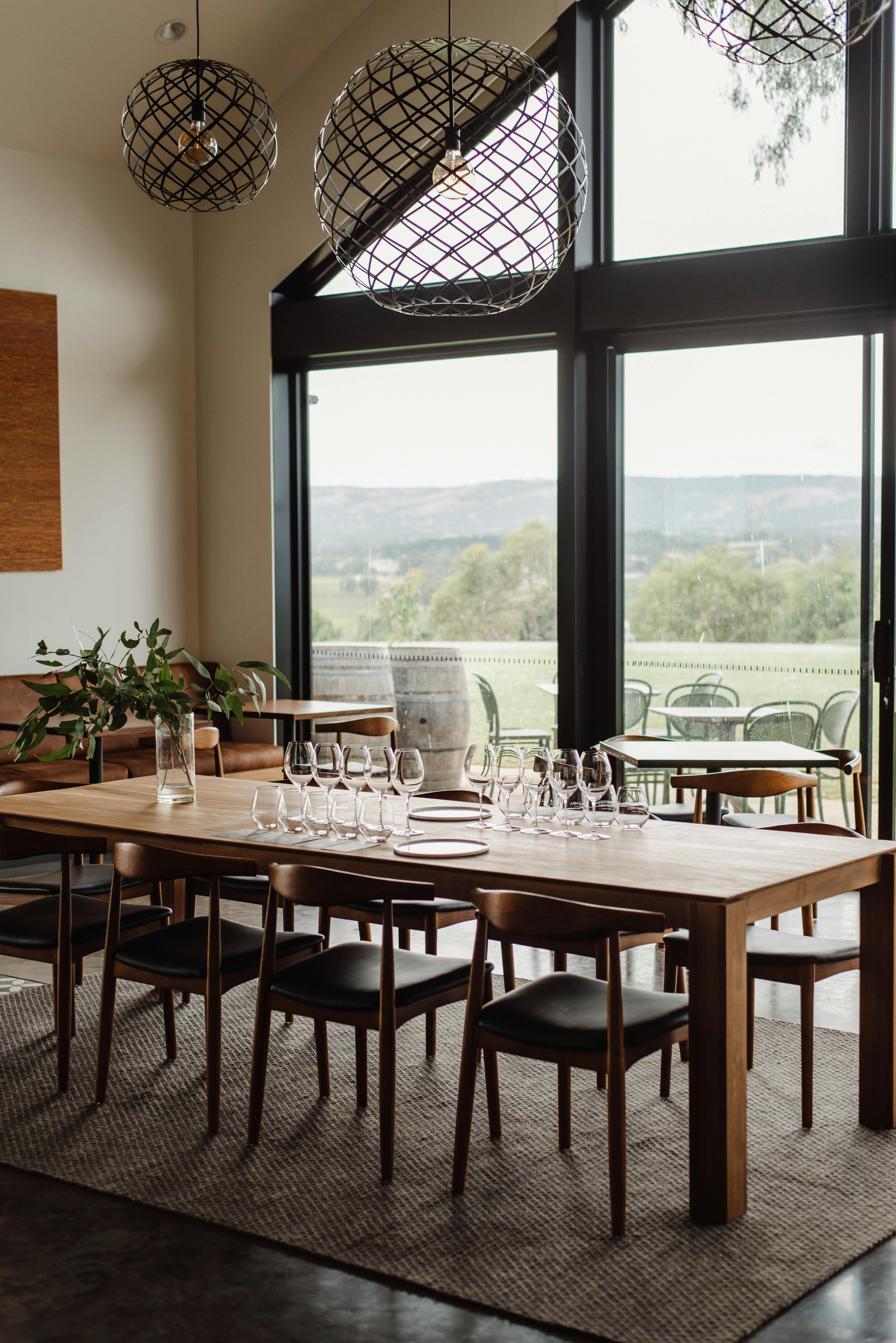 Large dining table set with glassware for a wine tasting experience, with window view in background