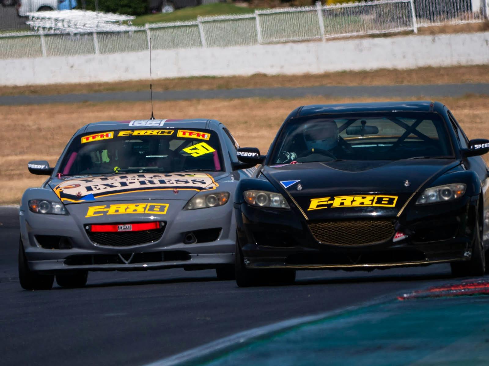 Two Mazda RX8s racing along a straight on a racetrack