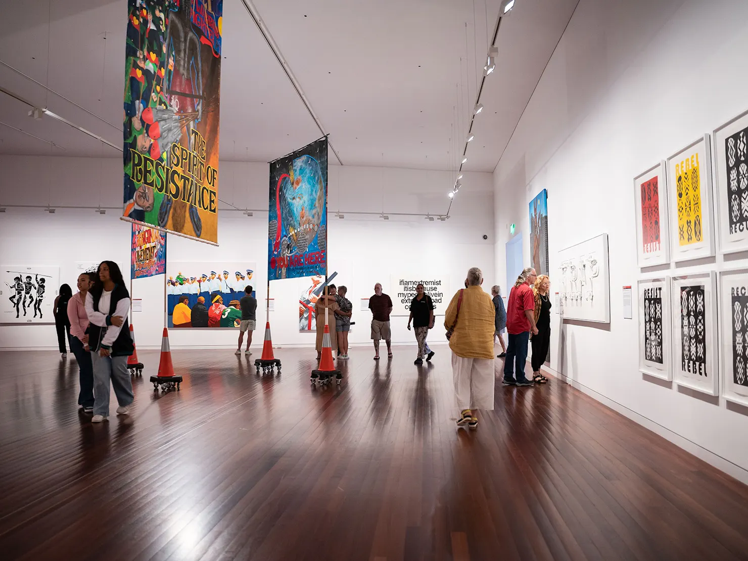 A group of people looking at geometric prints, large banners and paintings in a spacious gallery.