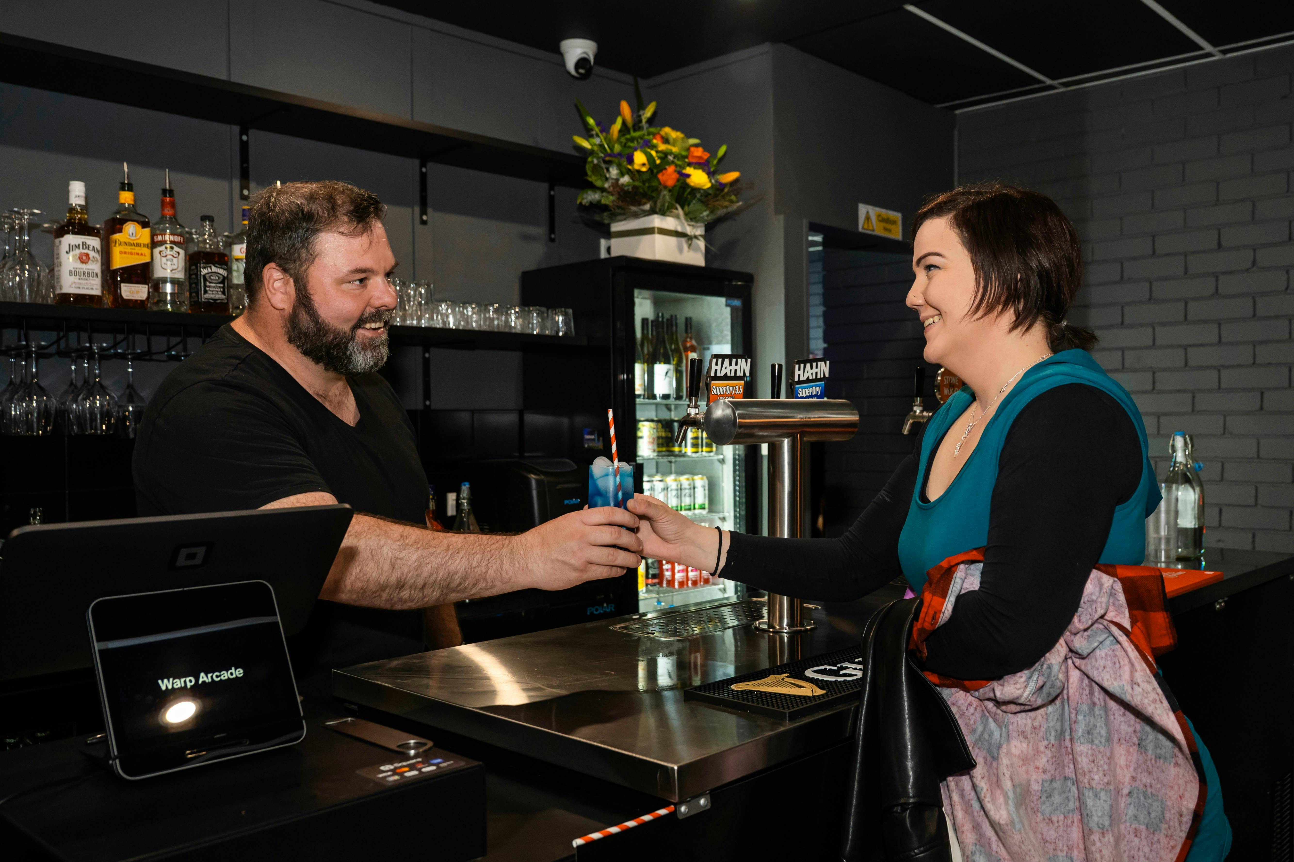 Bartender handling a drink to a customer inside the Warp Arcade bar