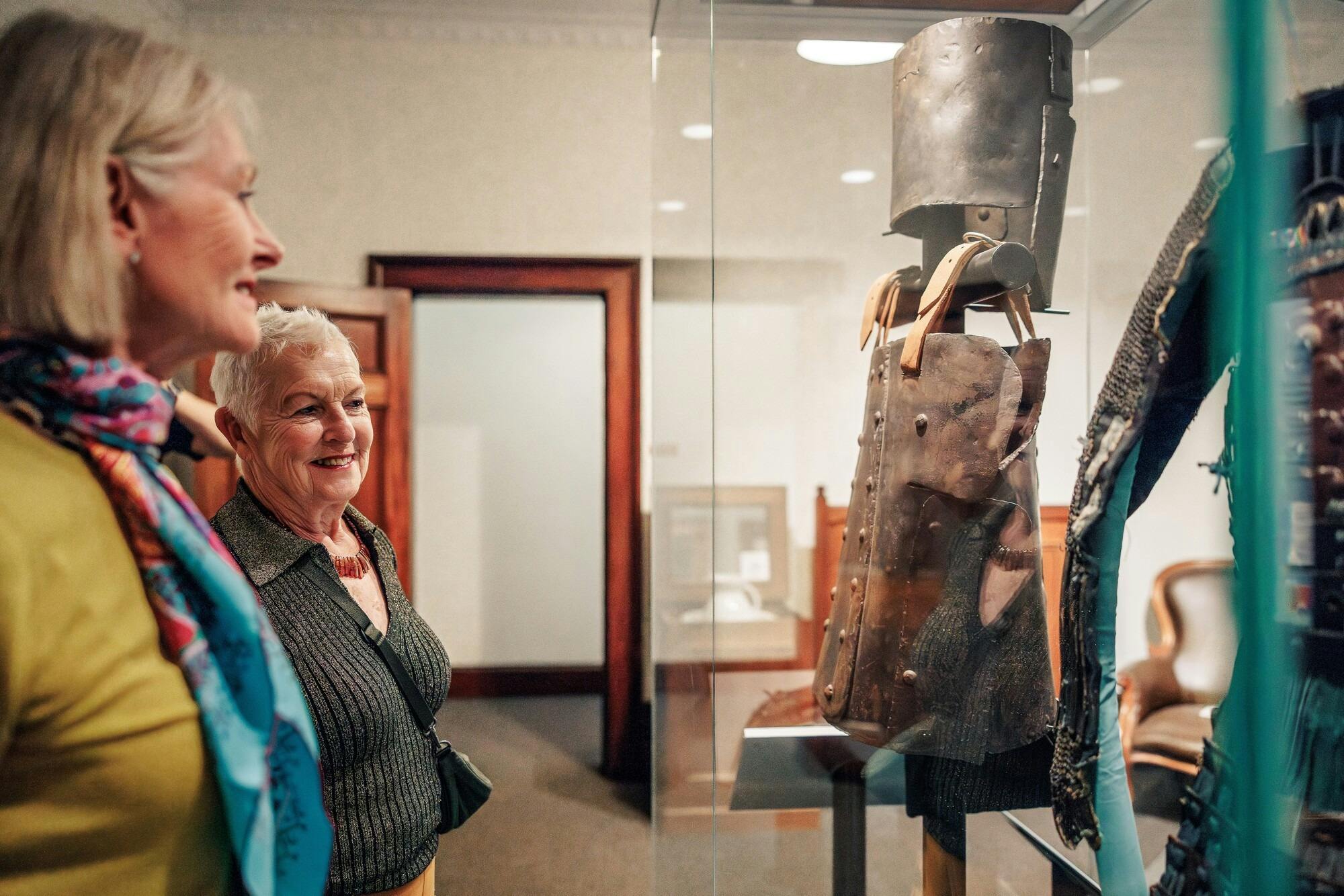 Two women in a museum looking at Ned Kelly armour in a glass cabinet