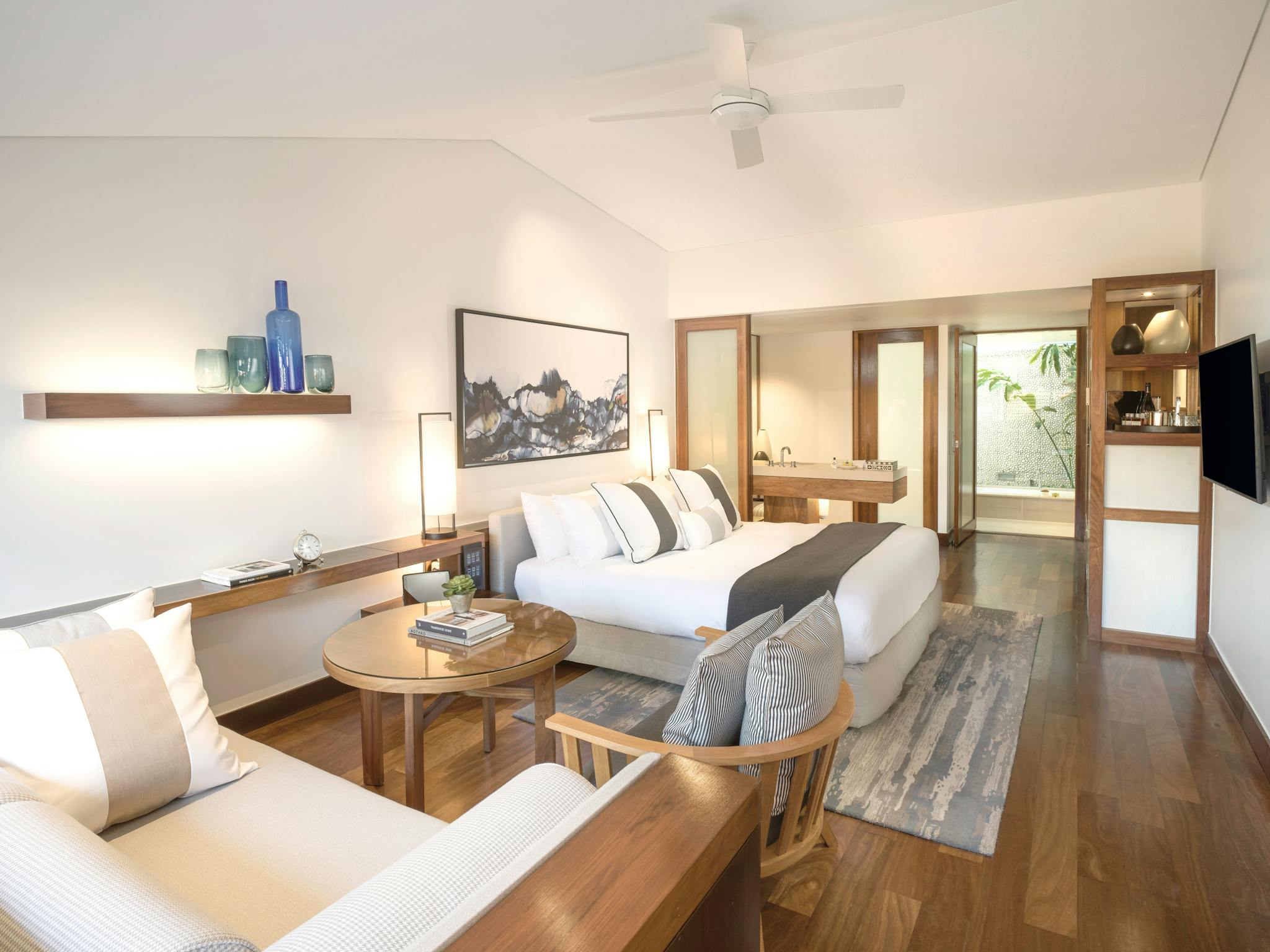 A luxurious bedroom with a king-sized bed, wooden furniture, seating area, and access to a glass-wal A luxurious bedroom with a king-sized bed, wooden furniture, seating area, and access to a glass-wal