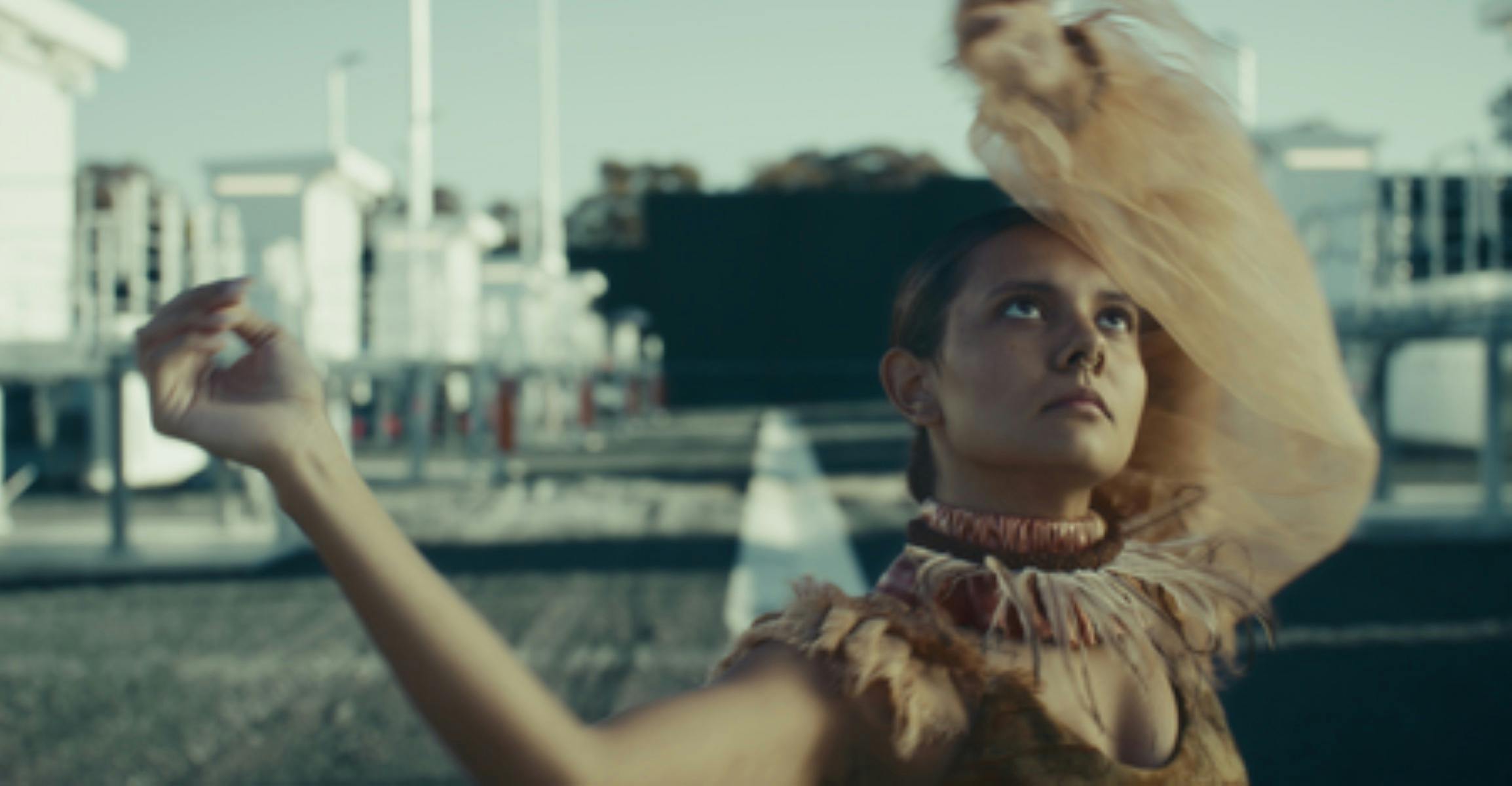 An image of a woman dancing with arms in the air, outdoors and looking toward the sky