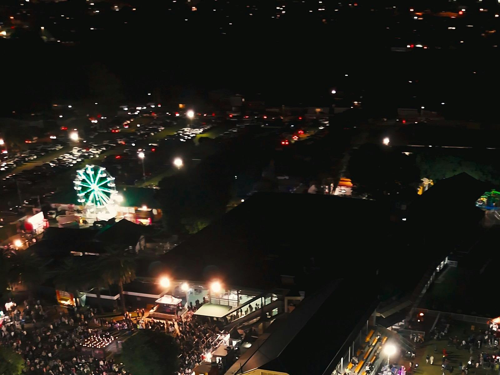 Night aerial view of a lit ferris wheel, car park, crowd and stalls at a past VIRAL festival