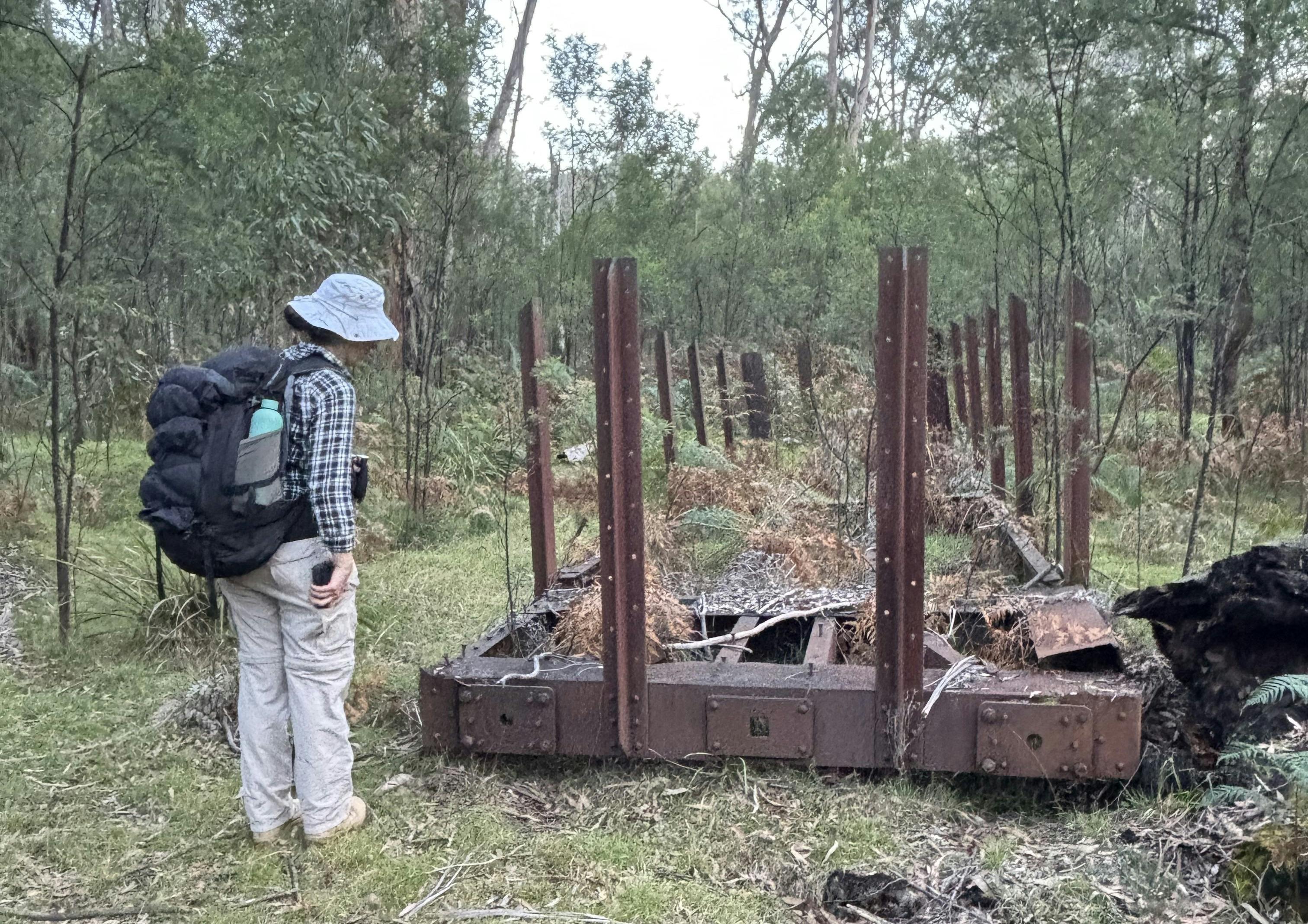 Woman stands next to the remains of a railway carriage in the Australian bush.