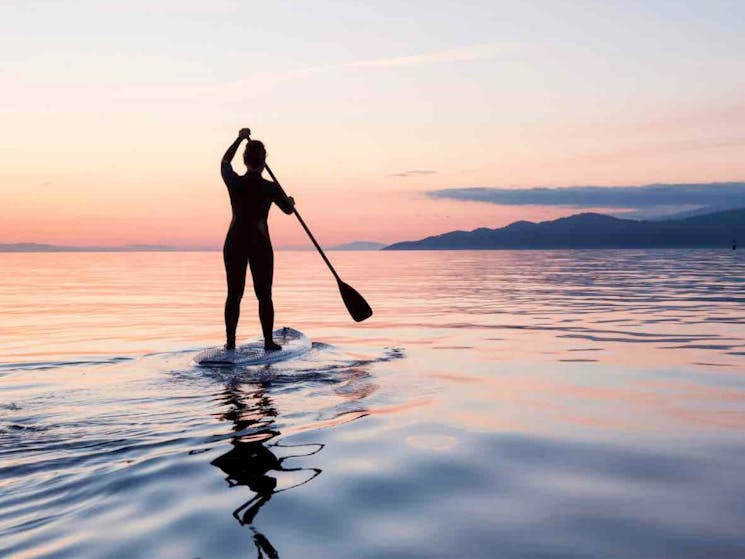Woman standing on a SUP at sunset.