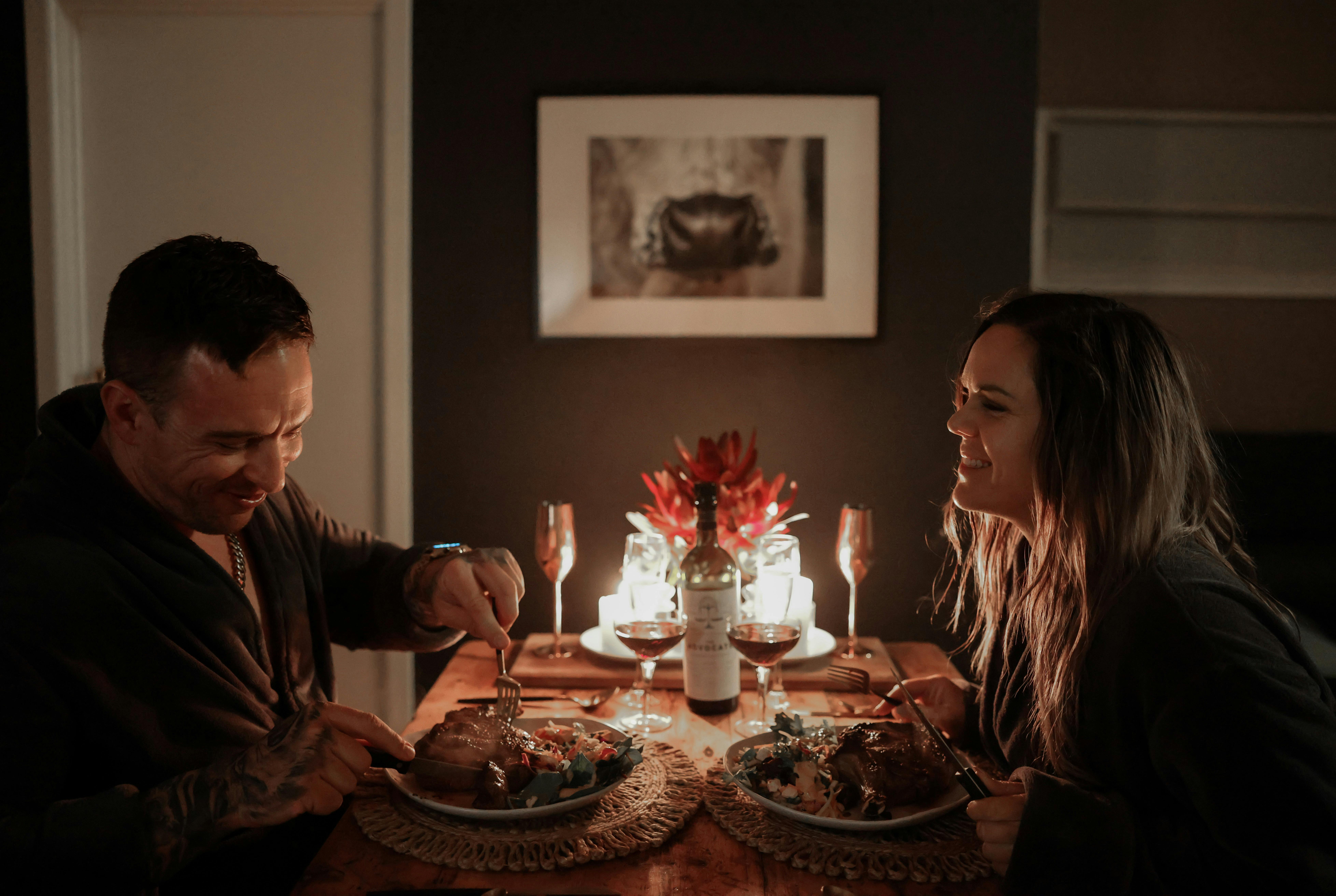 Couple enjoys dinner by candlelight on dining table, with meal they prepared in the cabin..