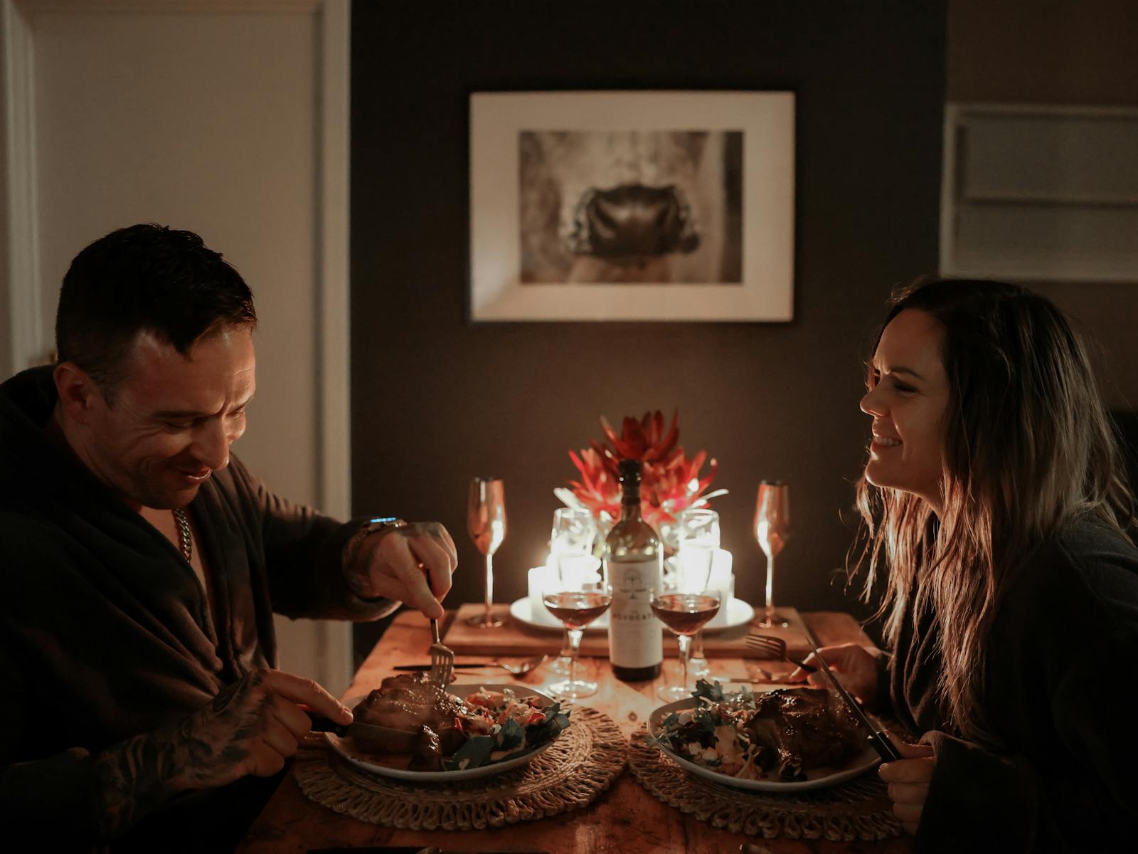 Couple enjoys dinner by candlelight on dining table, with meal they prepared in the cabin..
