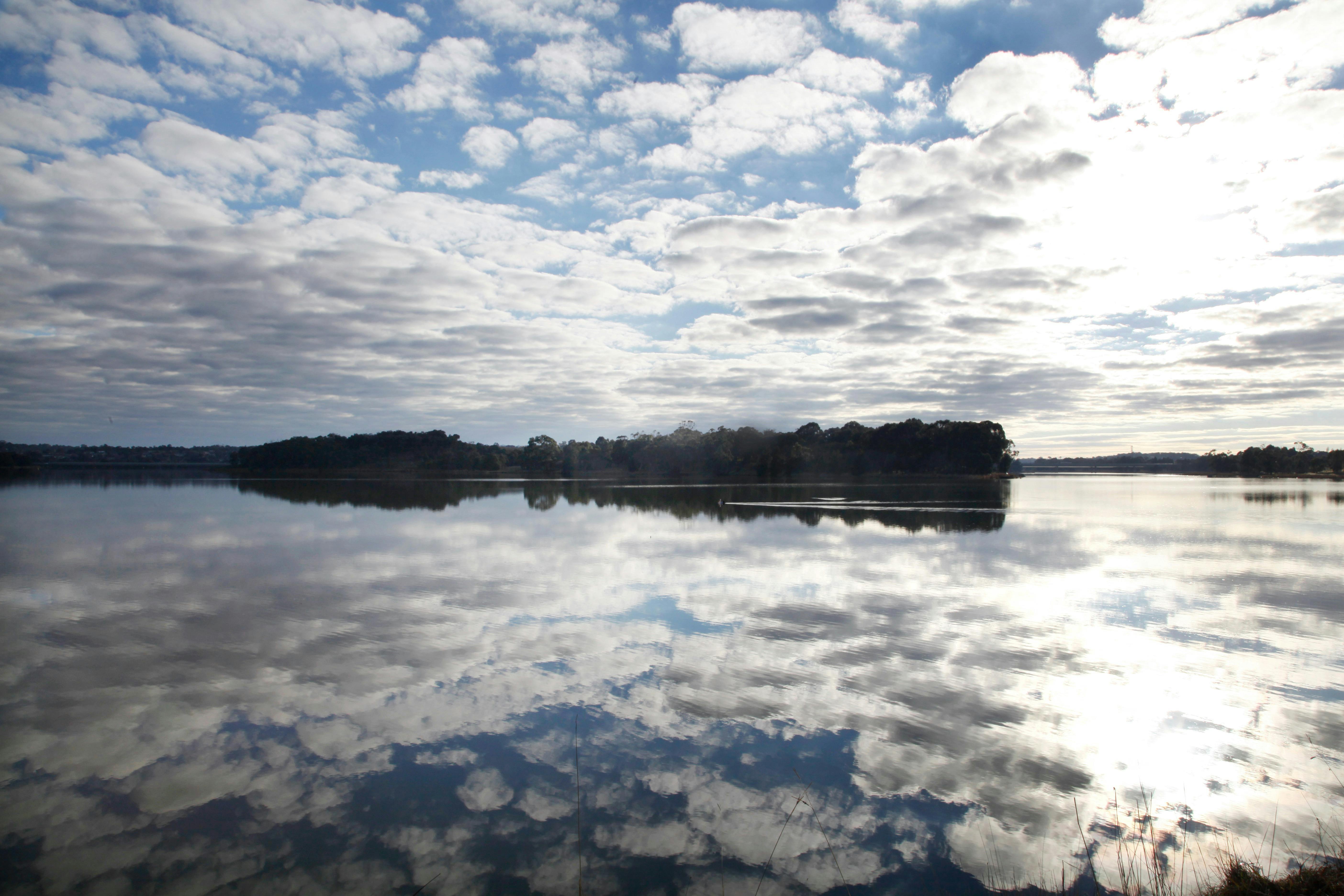 Lake Ginninderra on a sunlit day with clusters of clouds.