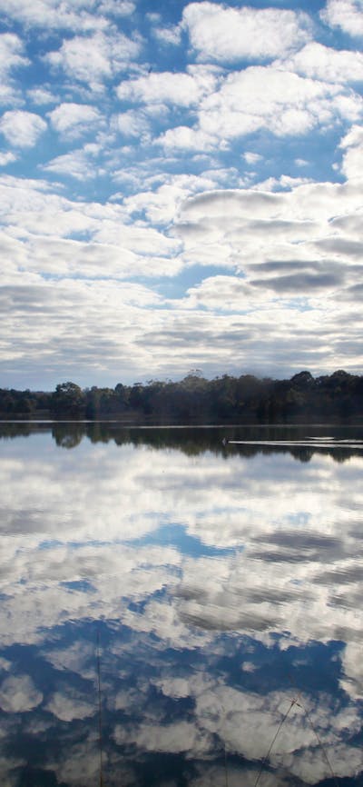 Lake Ginninderra on a sunlit day with clusters of clouds.