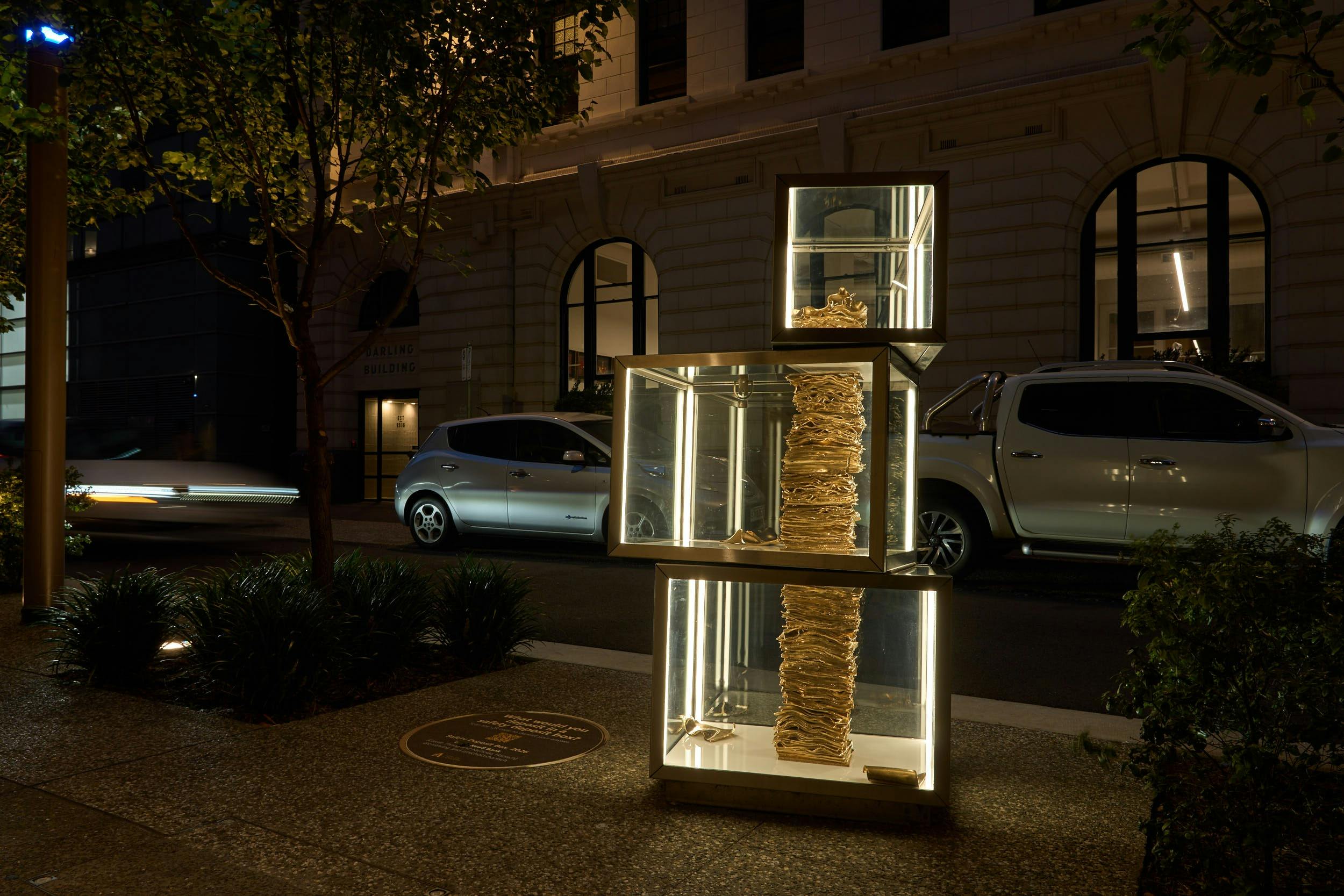 A stack of golden bank notes in a stack of glass boxes on the street at night.